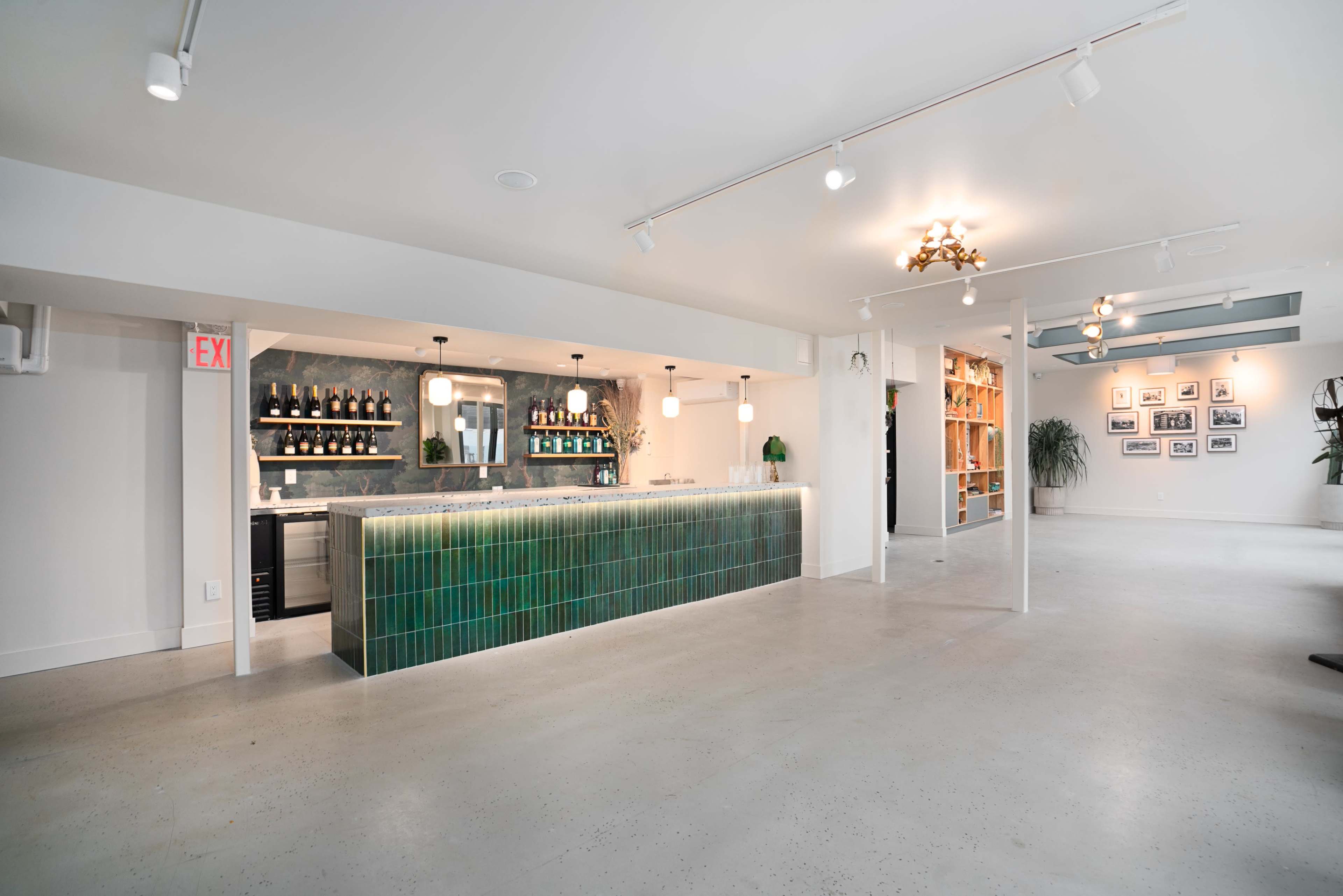 A modern, open space featuring a bar with a green tile front, shelves of wine bottles, and bookshelves along the walls.