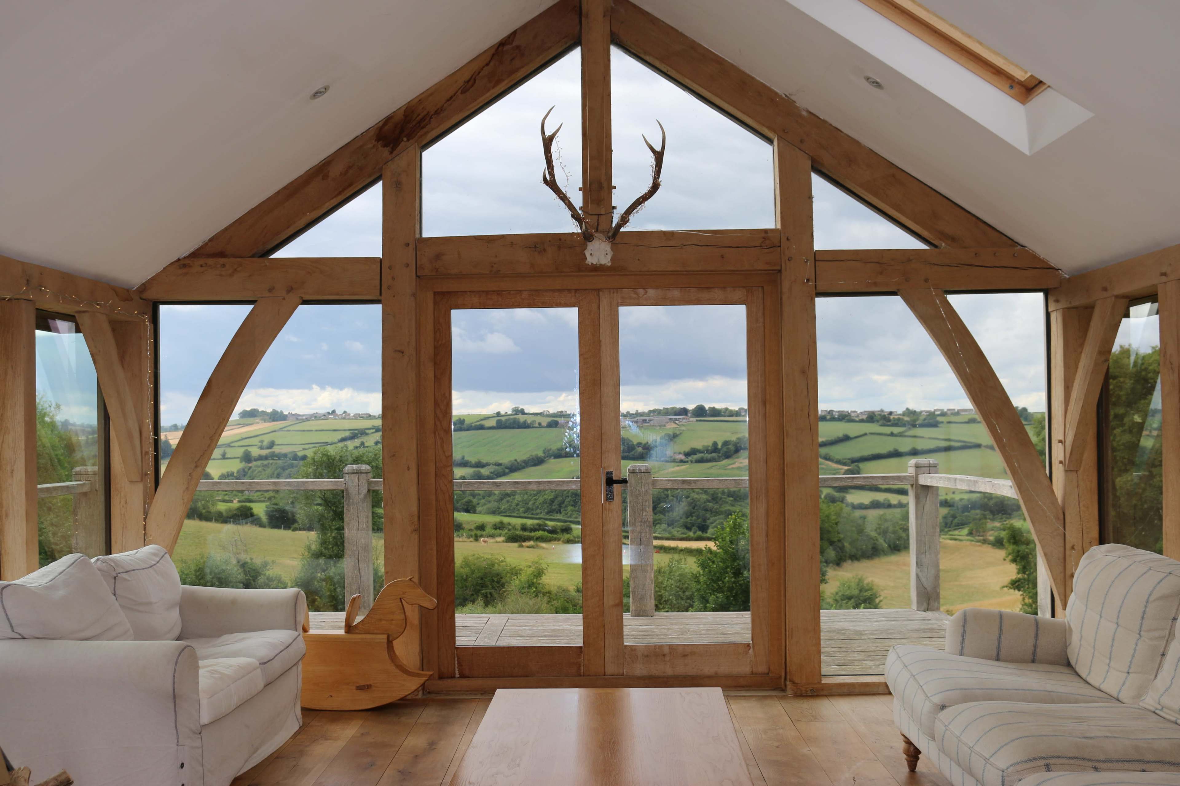 A wooden-framed room features large glass doors opening to a view of rolling green hills.