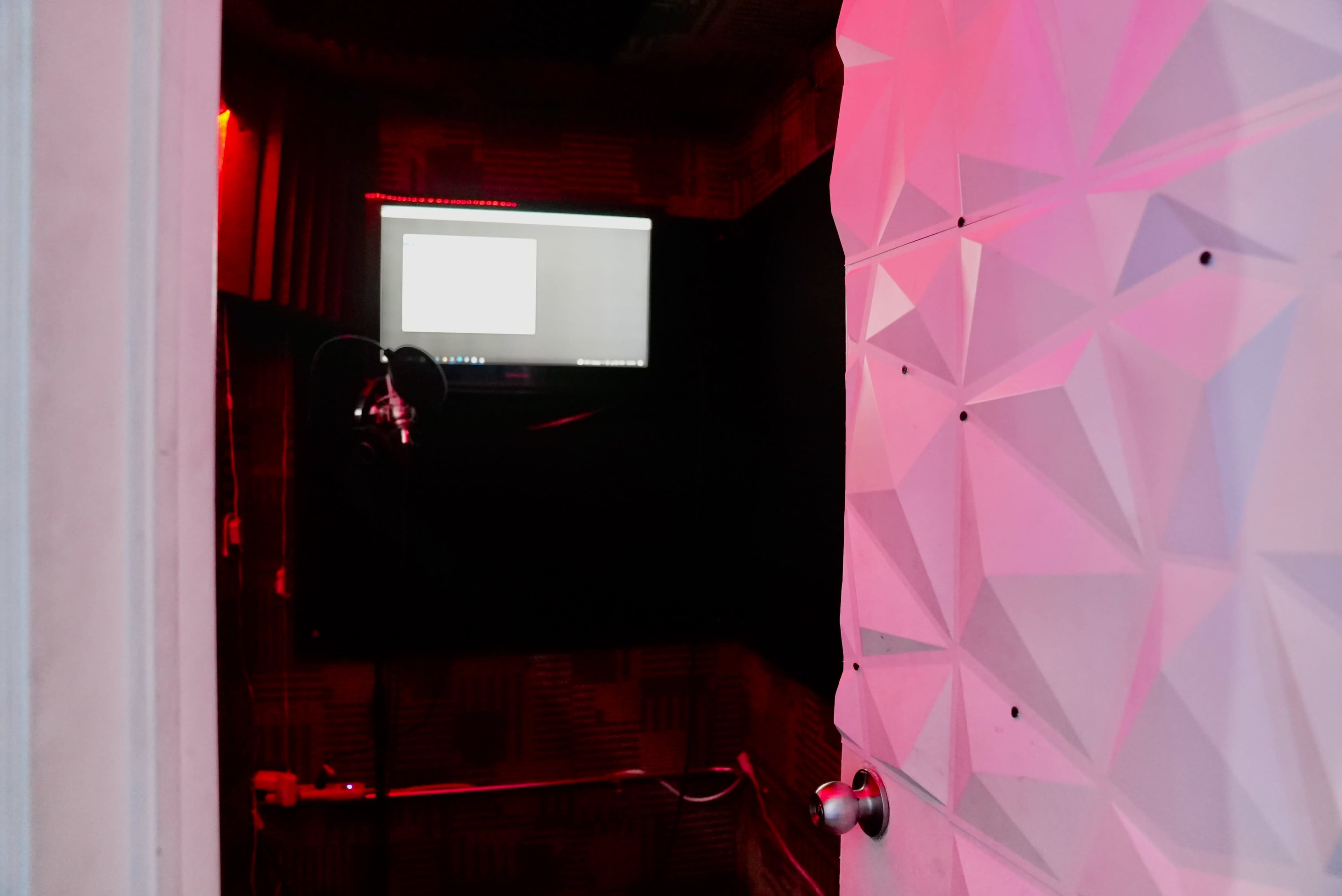 A soundproof recording booth with a computer screen and microphone visible inside.