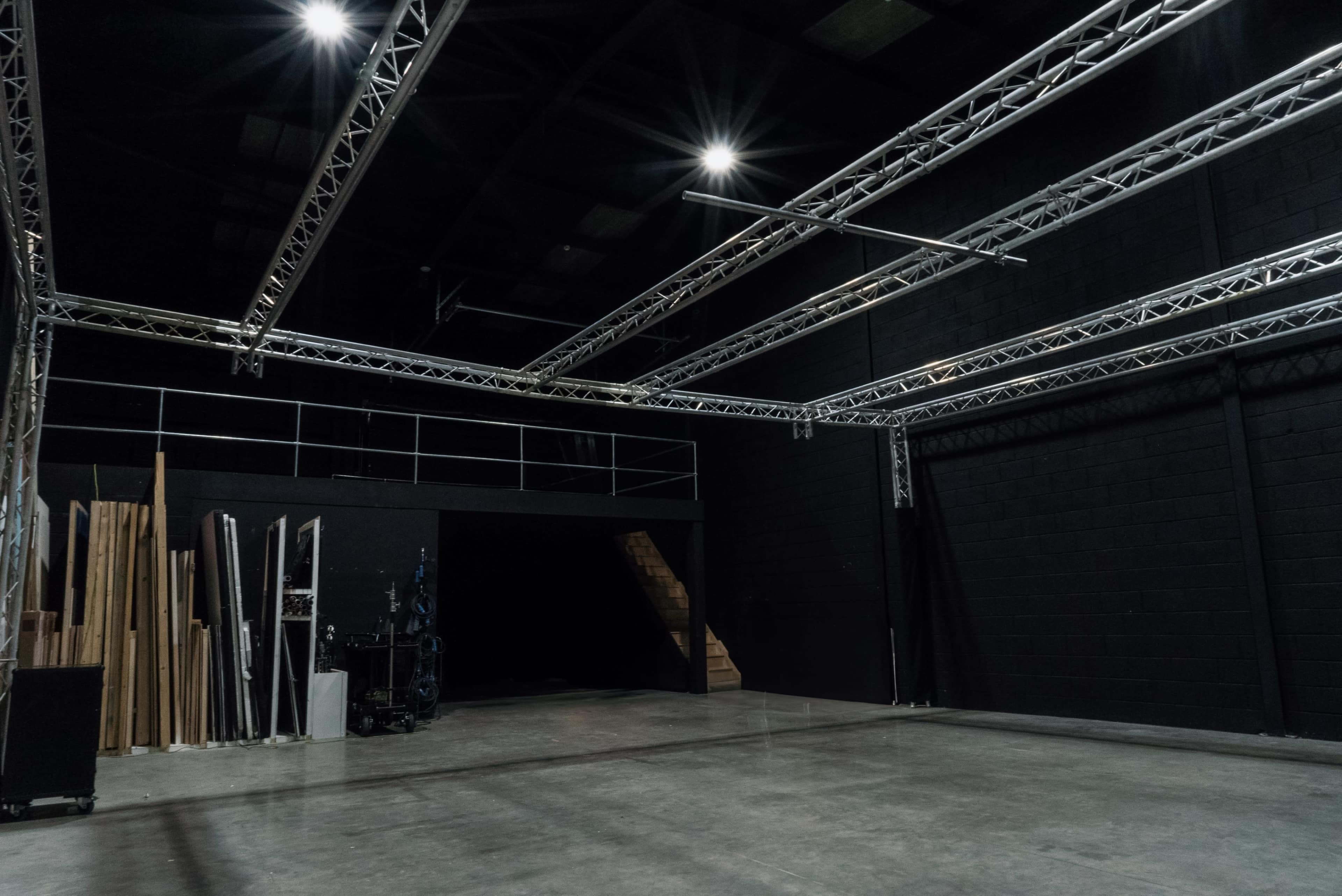 An empty industrial space with metal trusses overhead and wooden beams stacked against a black wall.
