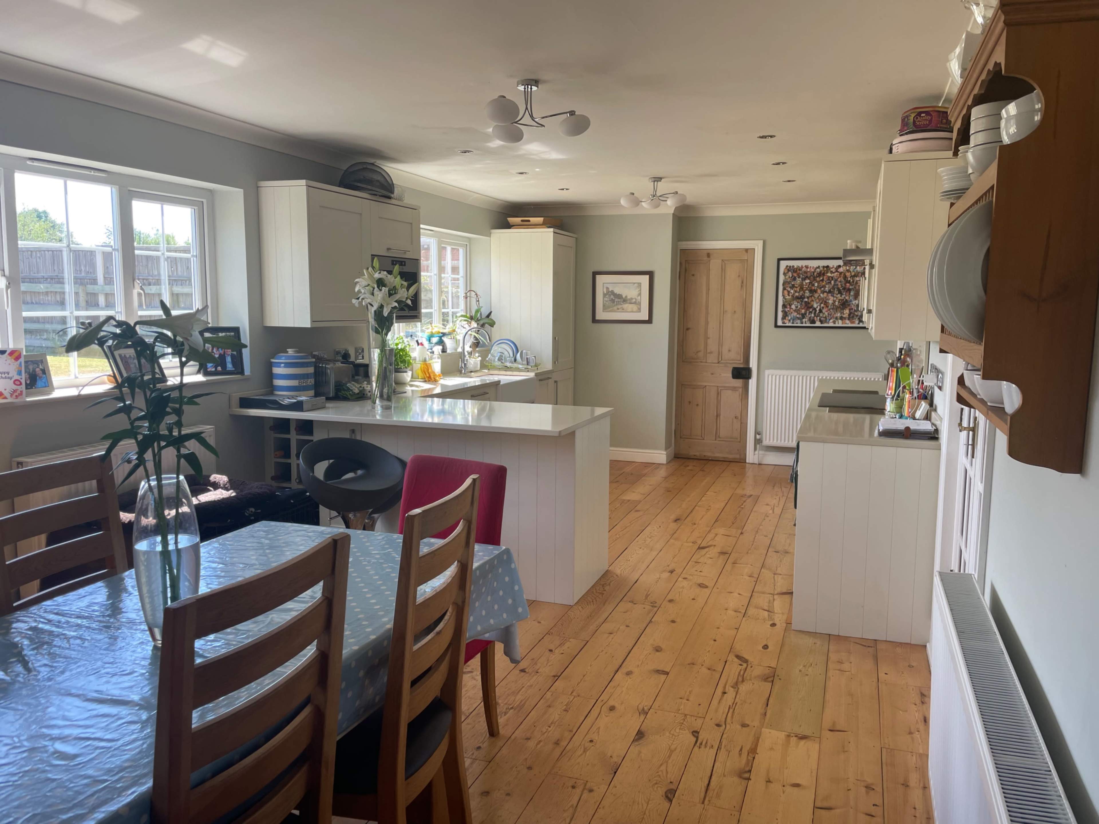 A brightly lit kitchen and dining area featuring wooden flooring, a table set for meals, and modern cabinetry.