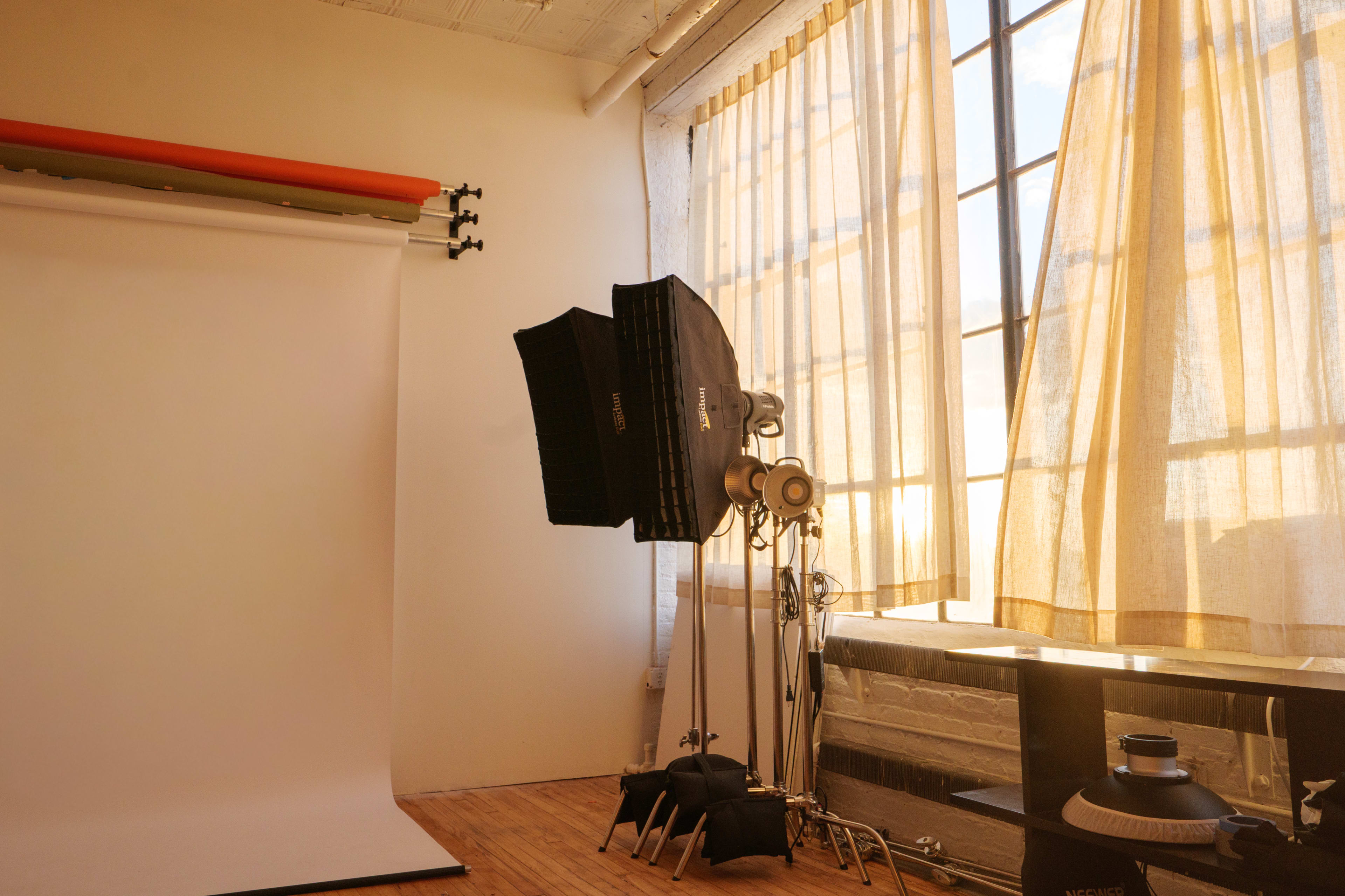The image shows a photography studio with a white backdrop, softbox lighting, and large windows covered by light curtains.
