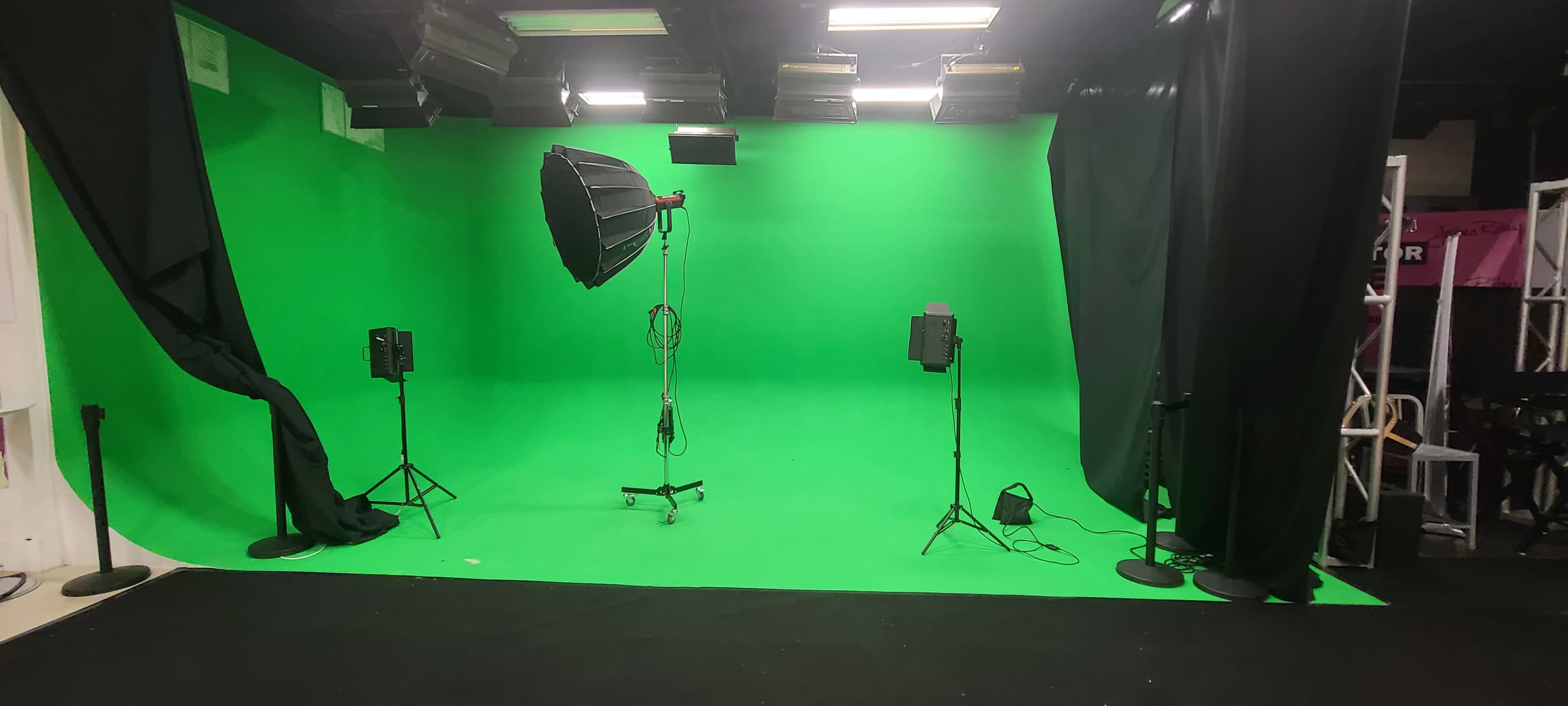 A green screen studio equipped with one large softbox light and two smaller lights on stands.