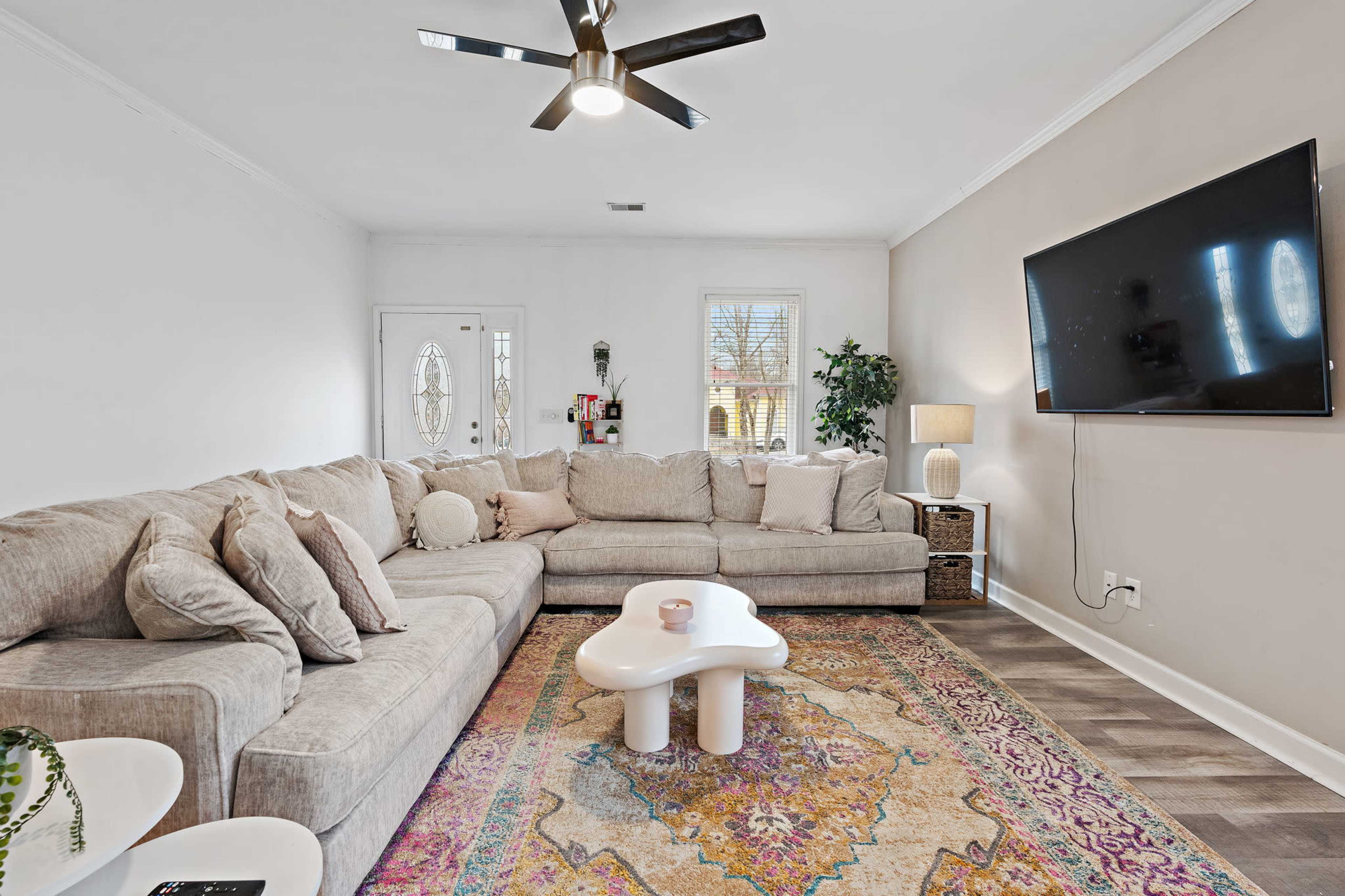 The spacious living room features a large sectional sofa, a decorative area rug, a modern coffee table, and a wall-mounted television.