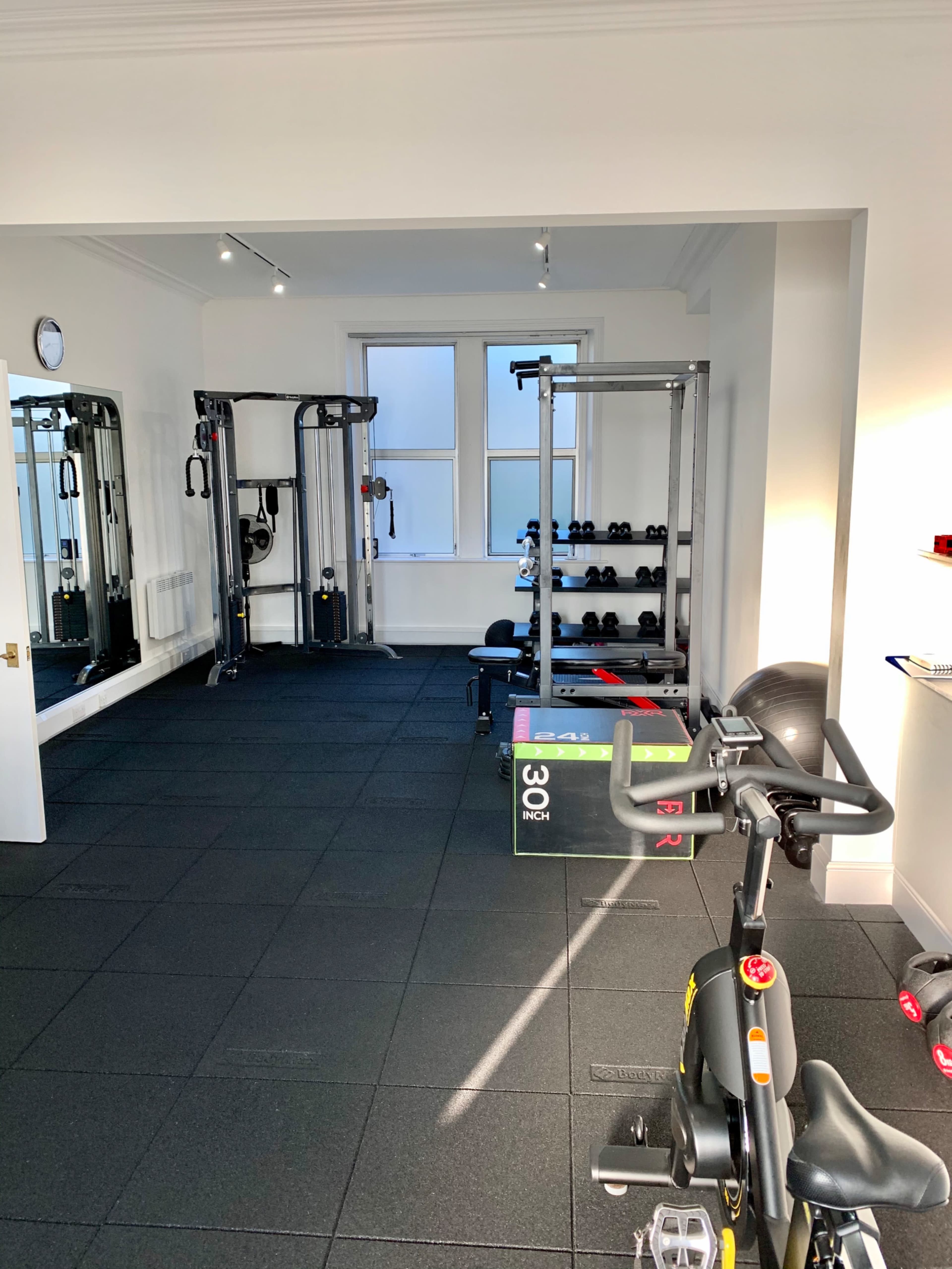 The image shows a well-equipped home gym featuring a stationary bike, weight racks, and a multi-function strength training machine.