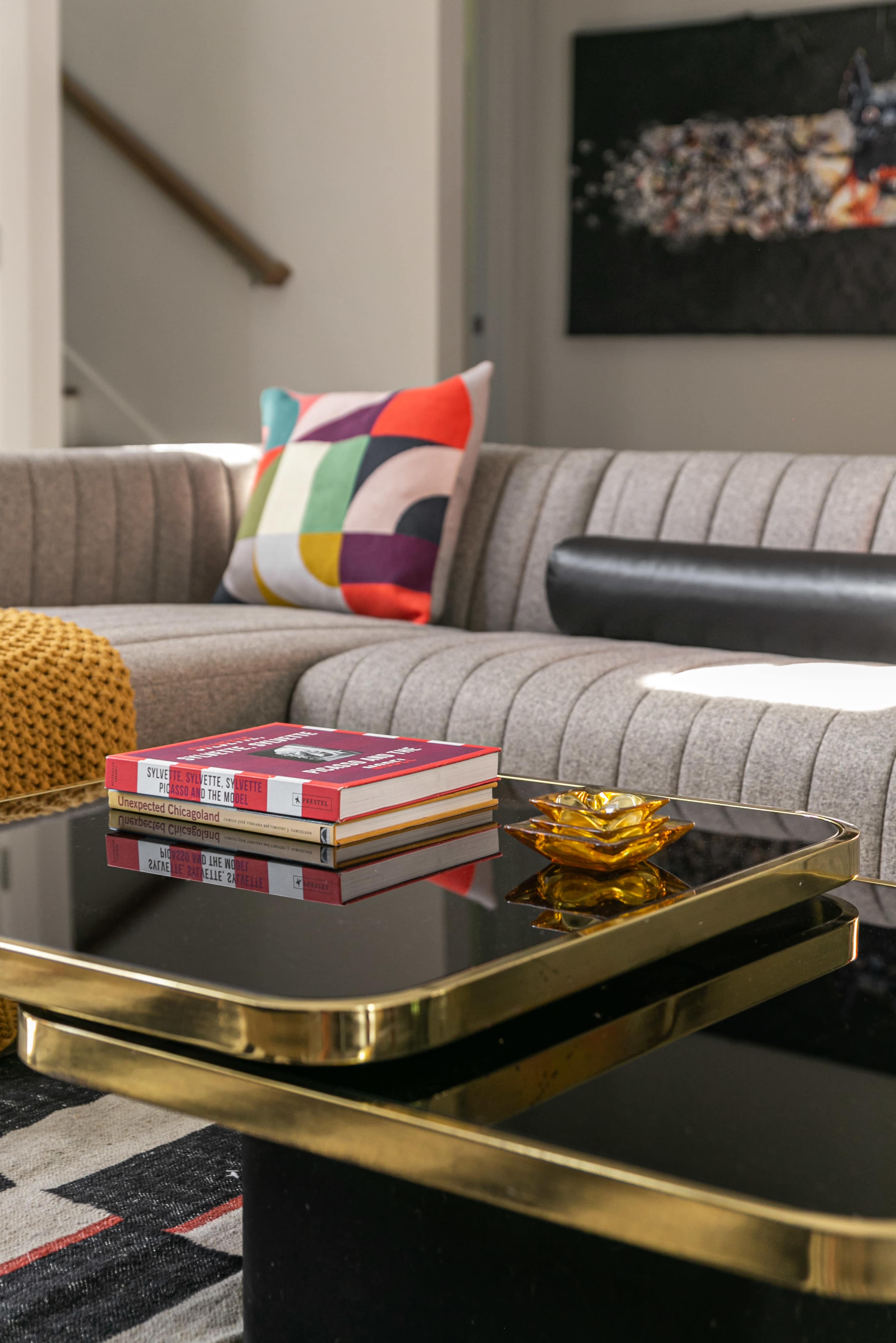 A modern living room scene features a gray striped sofa with a colorful cushion, a gold-accented black coffee table holding books and a decorative object.