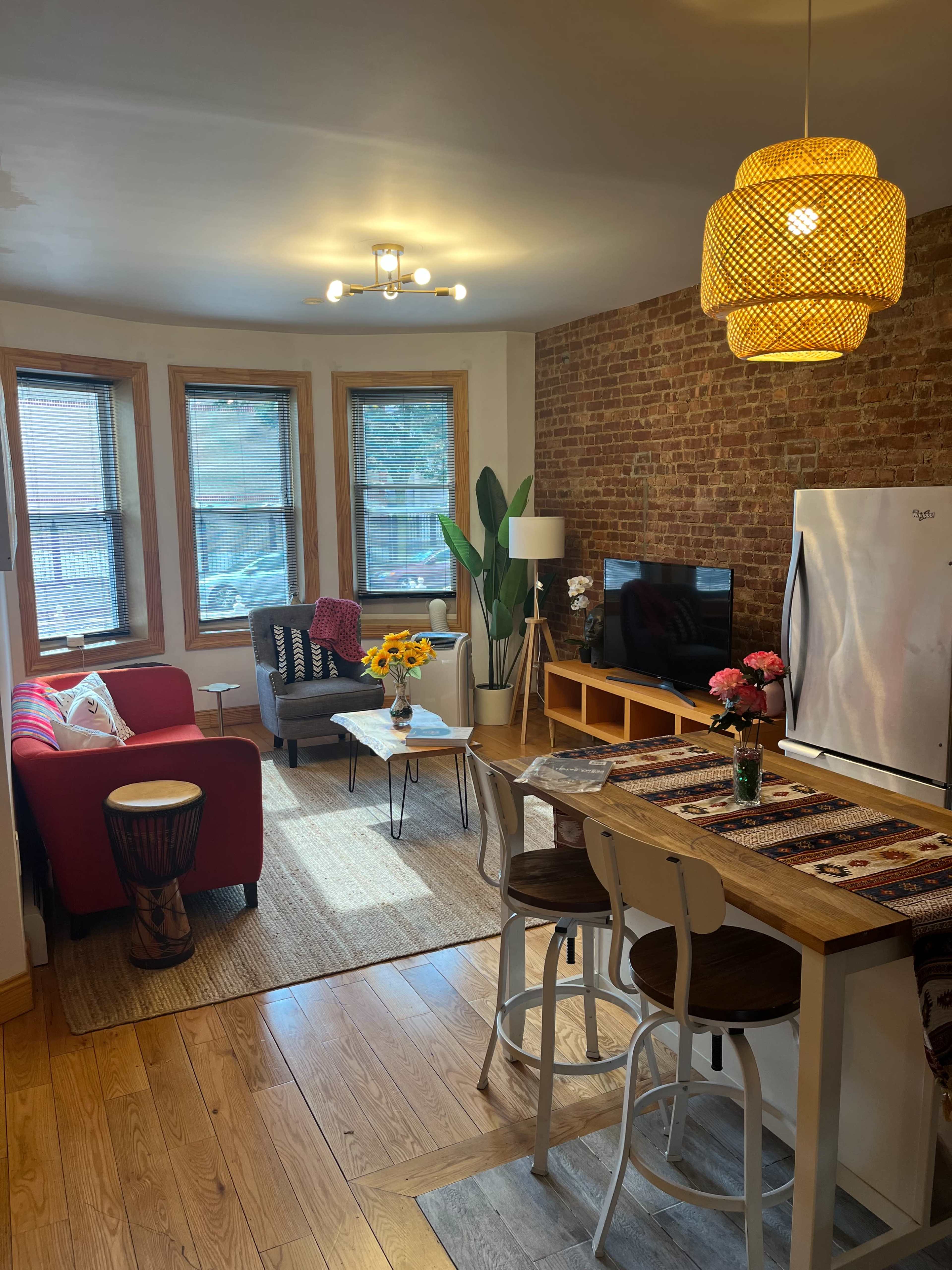 A cozy living space with a red sofa, a dining table with white chairs, and wooden floors, accented by a large potted plant and a TV.