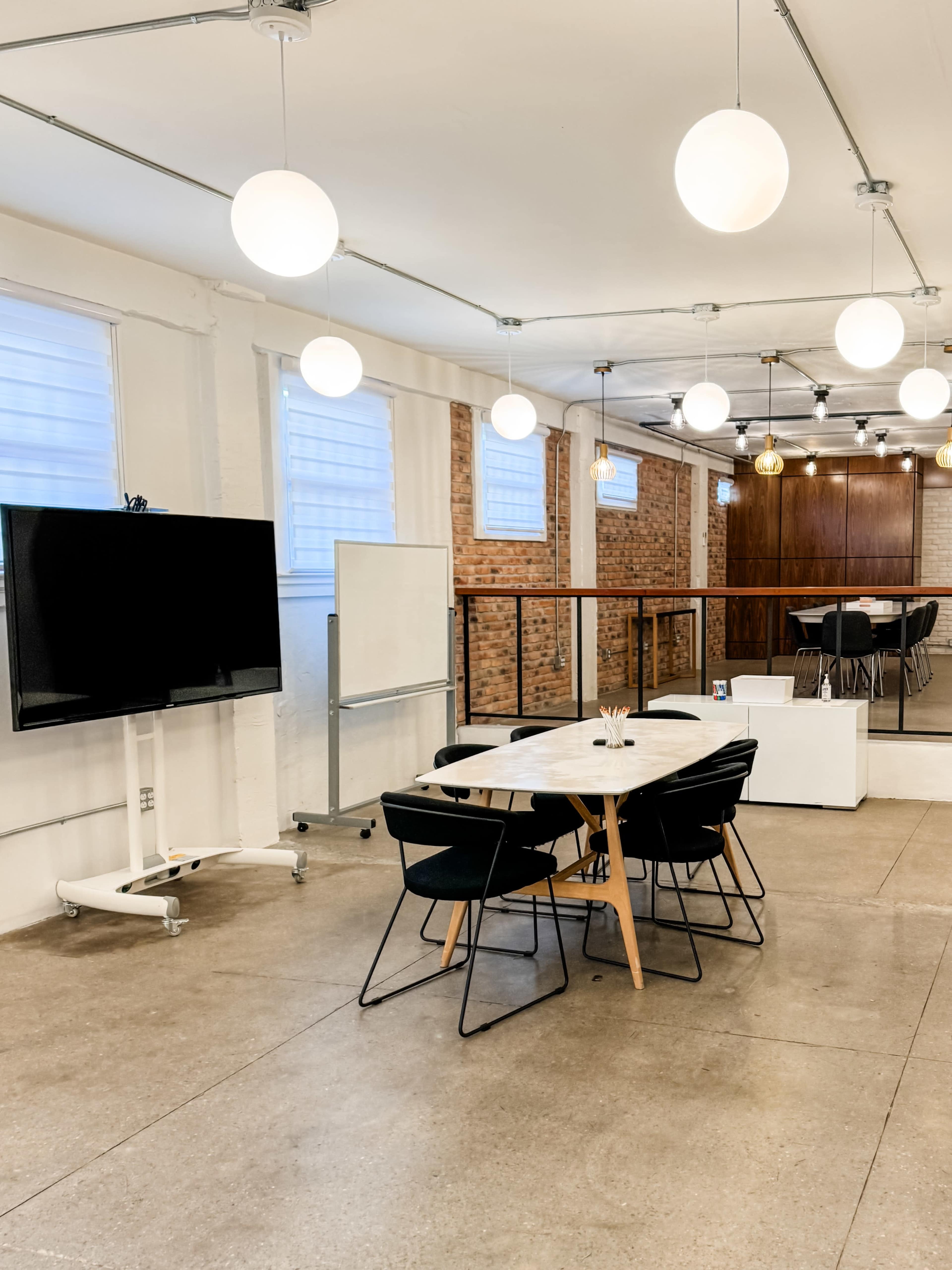 A modern meeting room features a large marble table surrounded by black chairs, with a television and whiteboard on one side and wooden cabinetry in the background.