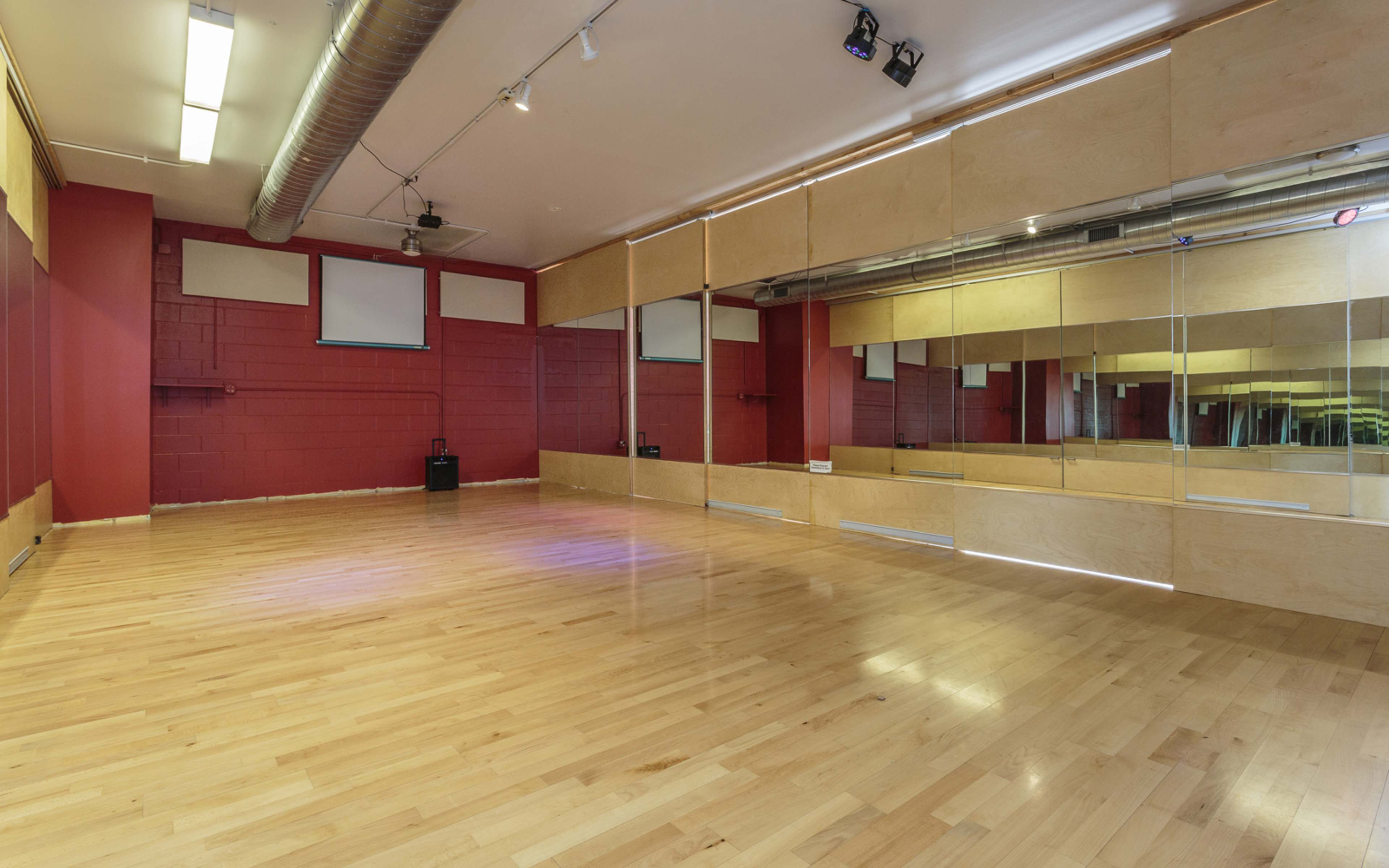 A spacious dance studio with hardwood flooring, red walls, and large mirrors along one side.