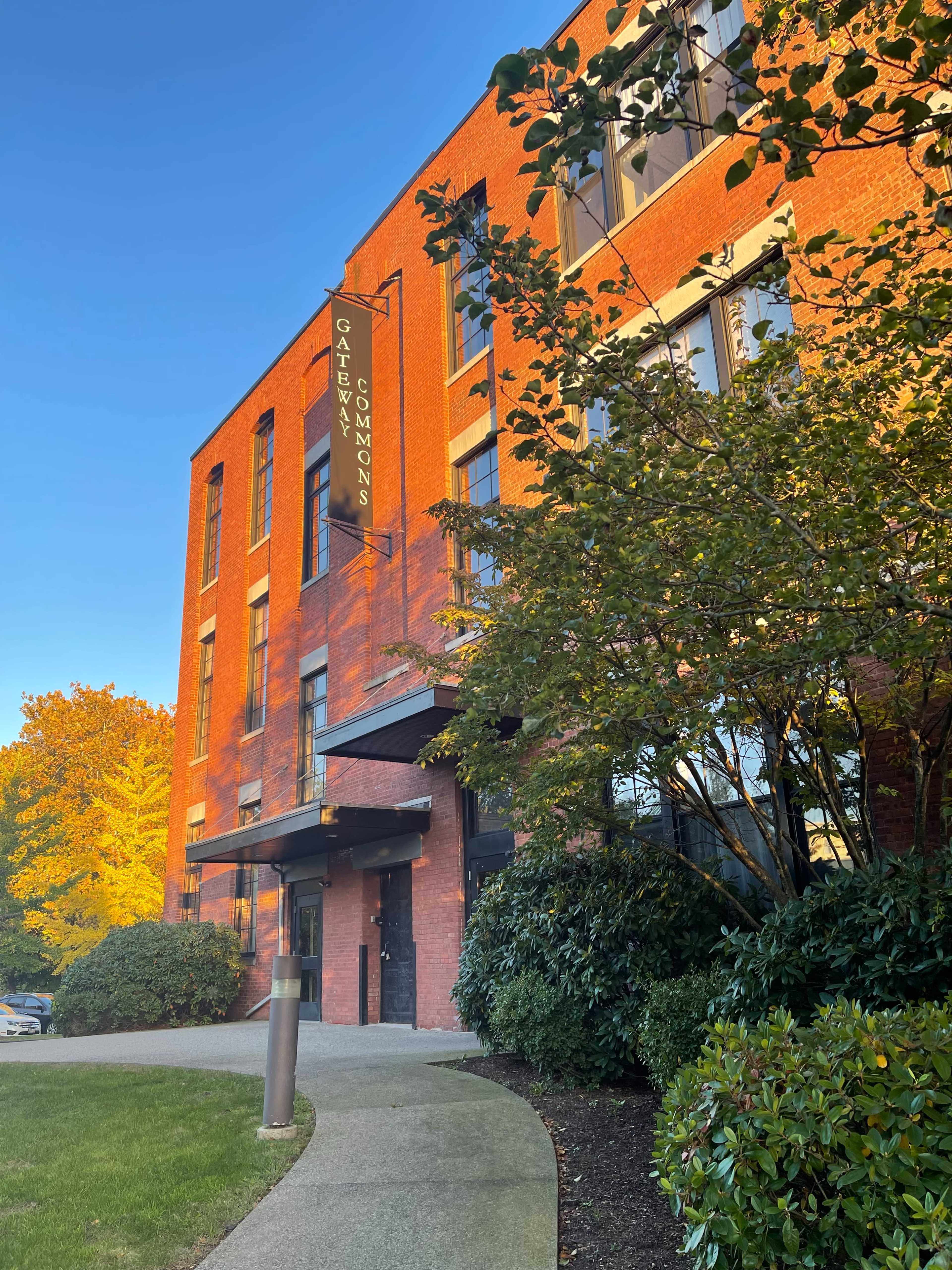The image shows a brick building labeled "Gateway Commons" surrounded by greenery and autumn-colored trees.