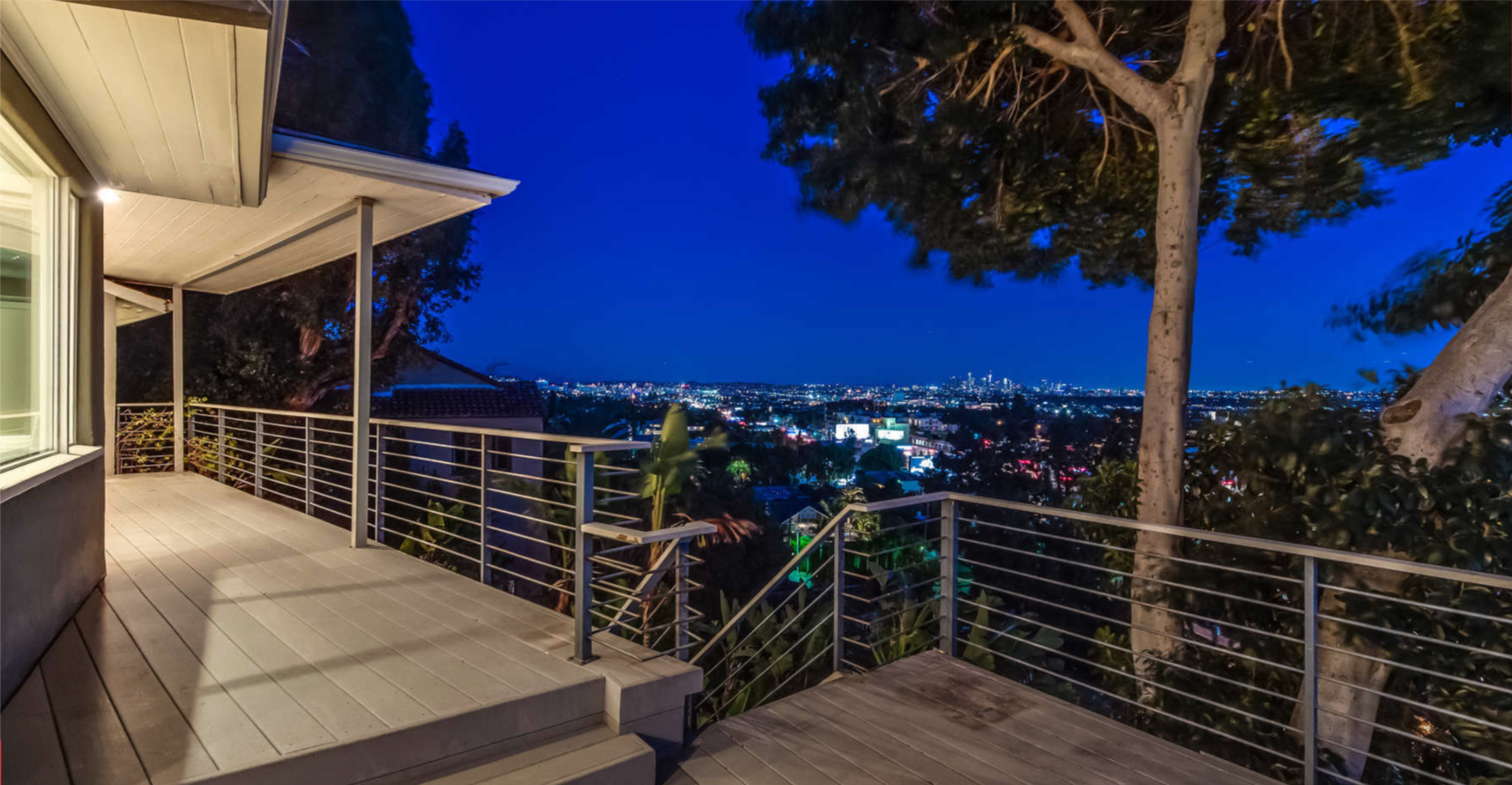 The image shows a deck with a railing overlooking a city skyline at night.