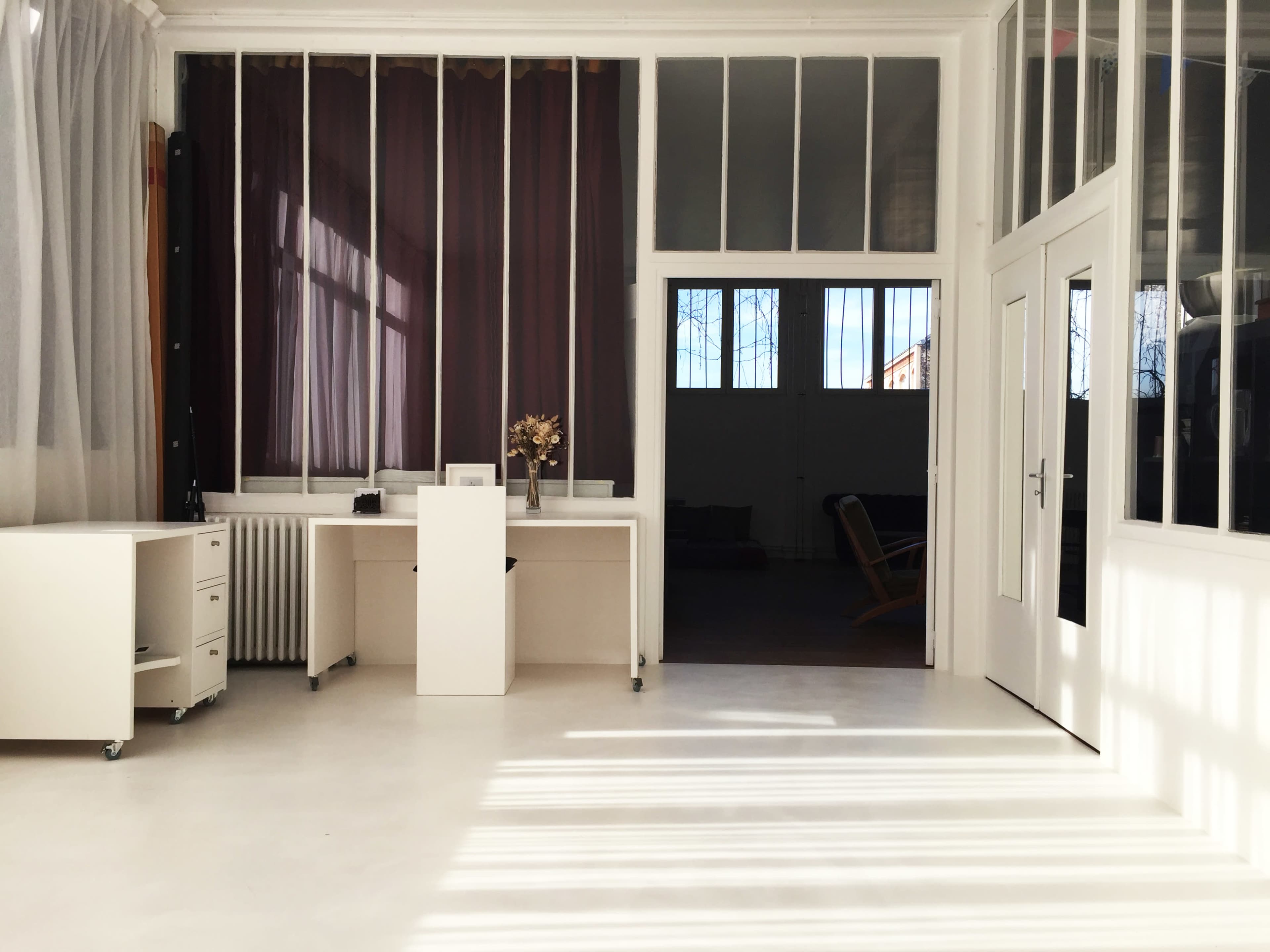 A bright, minimalistic office space with large windows, light-colored furniture, and a clean floor.