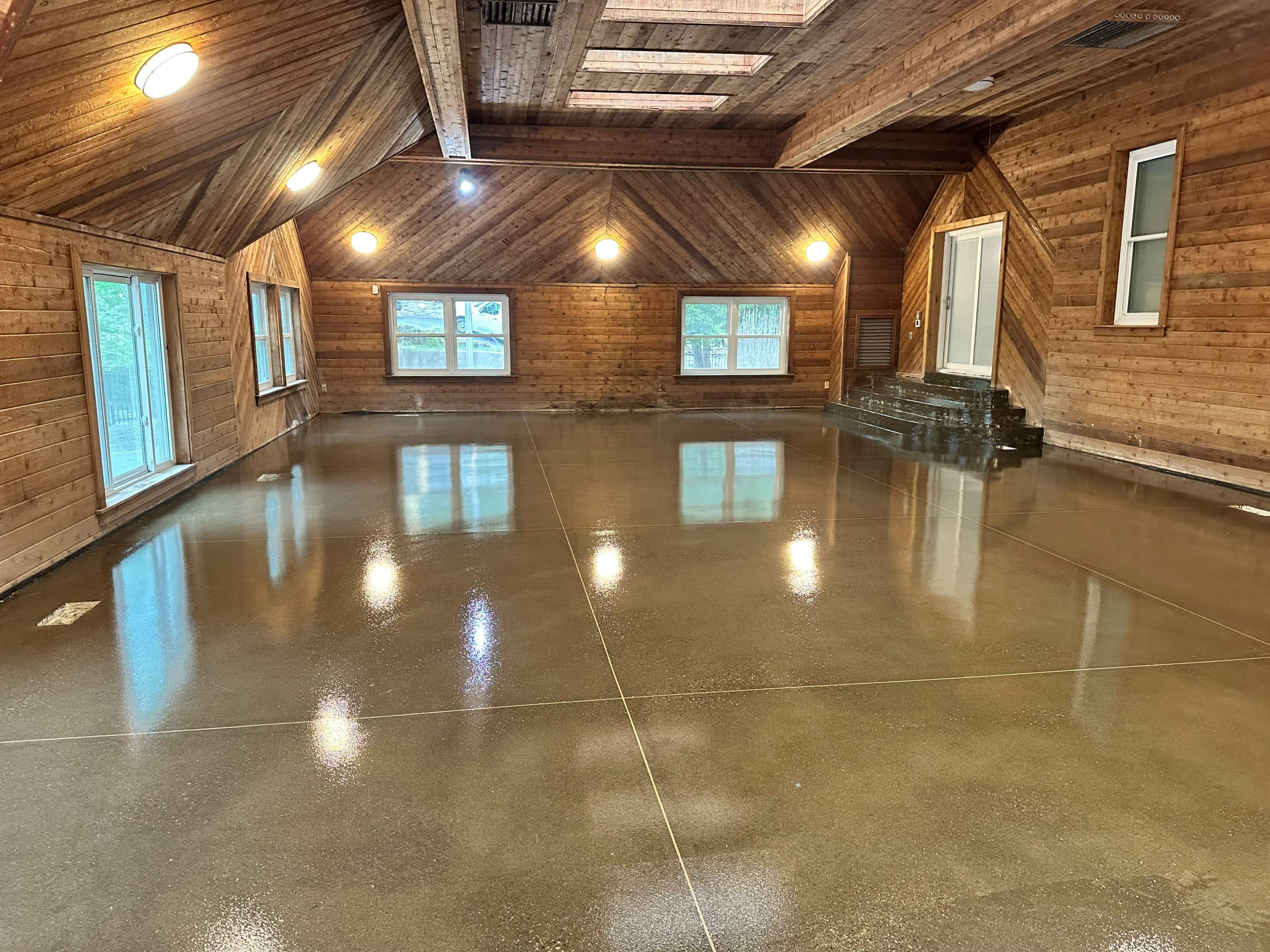An empty room with wooden walls and a polished concrete floor, illuminated by overhead lights.