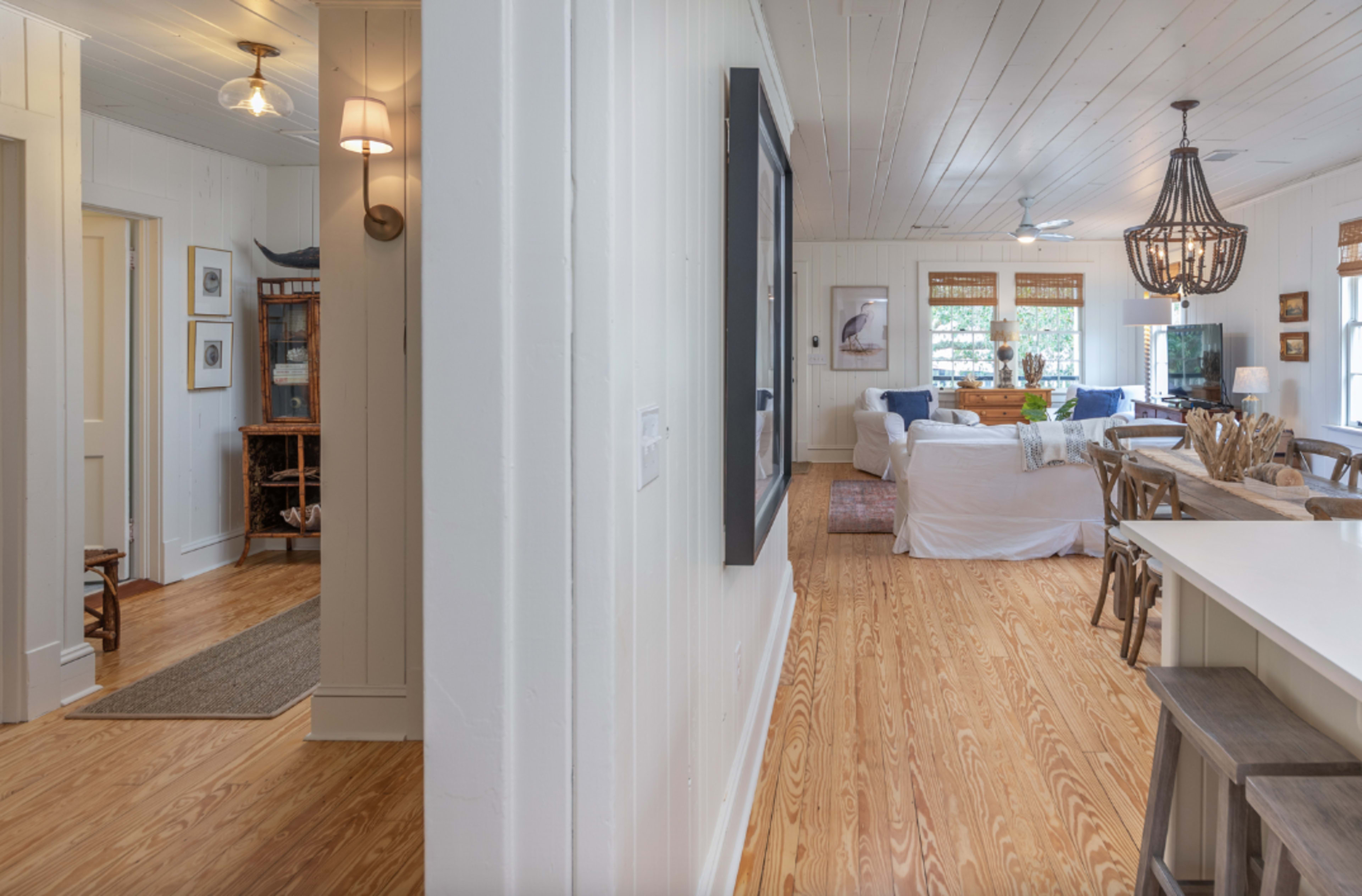 A bright and open interior space with a view of a living area connected to a dining area, featuring wooden floors and light-colored walls.