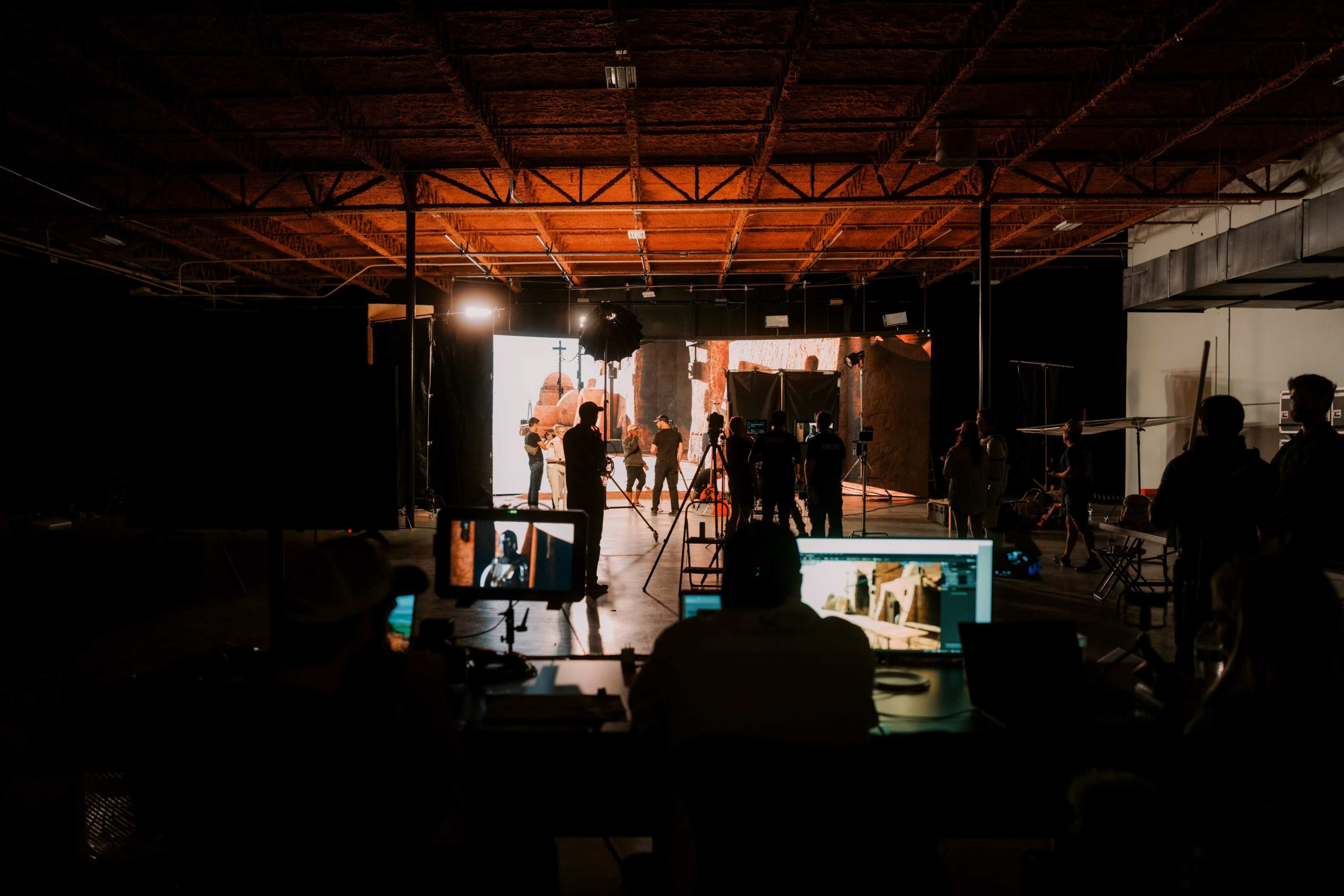 A film production set is illuminated with various lights as crew members operate cameras and monitors in a dimly lit space.