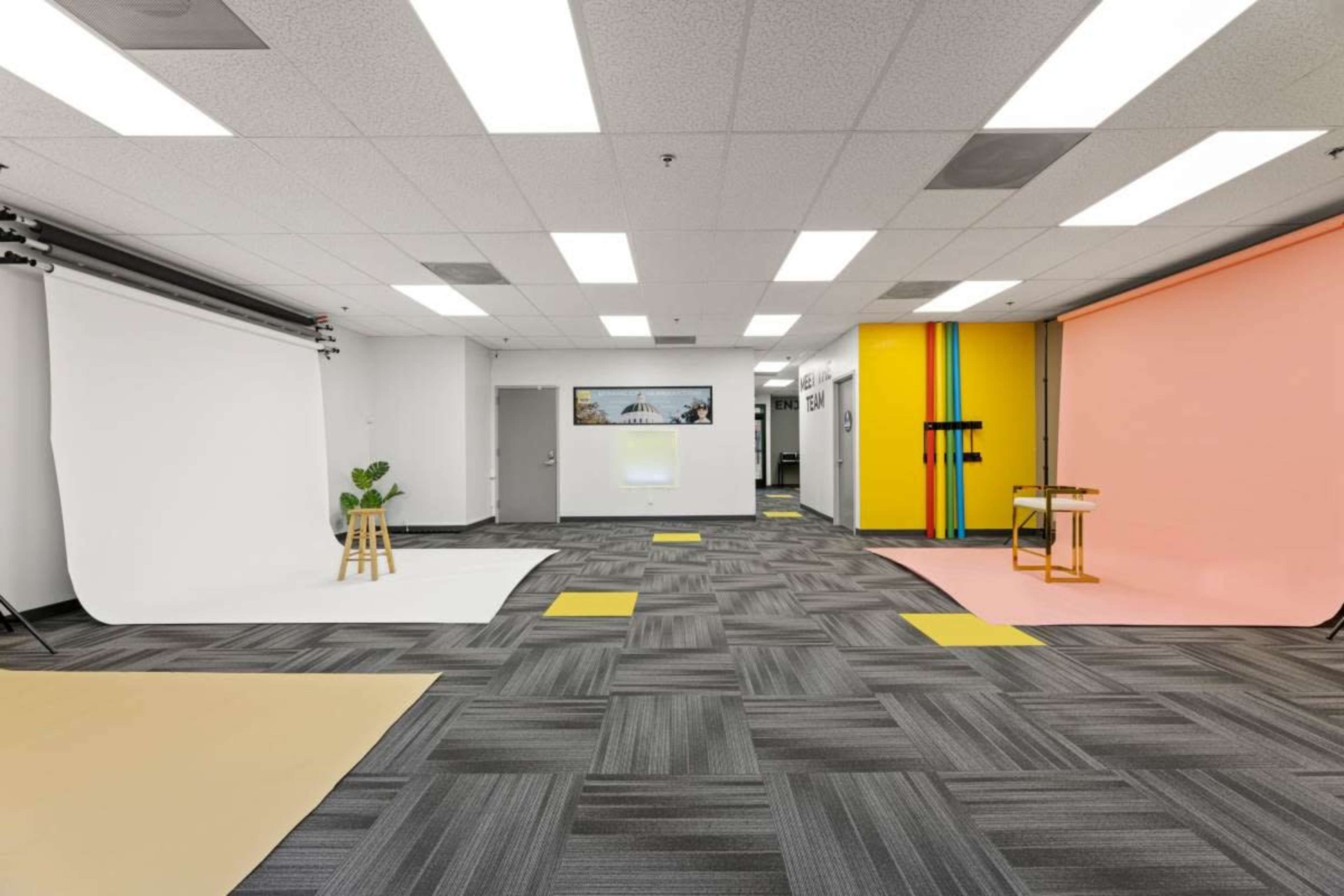 The image shows a spacious studio with various backdrops, including a white, pink, and yellow wall, along with modern flooring and lighting fixtures.
