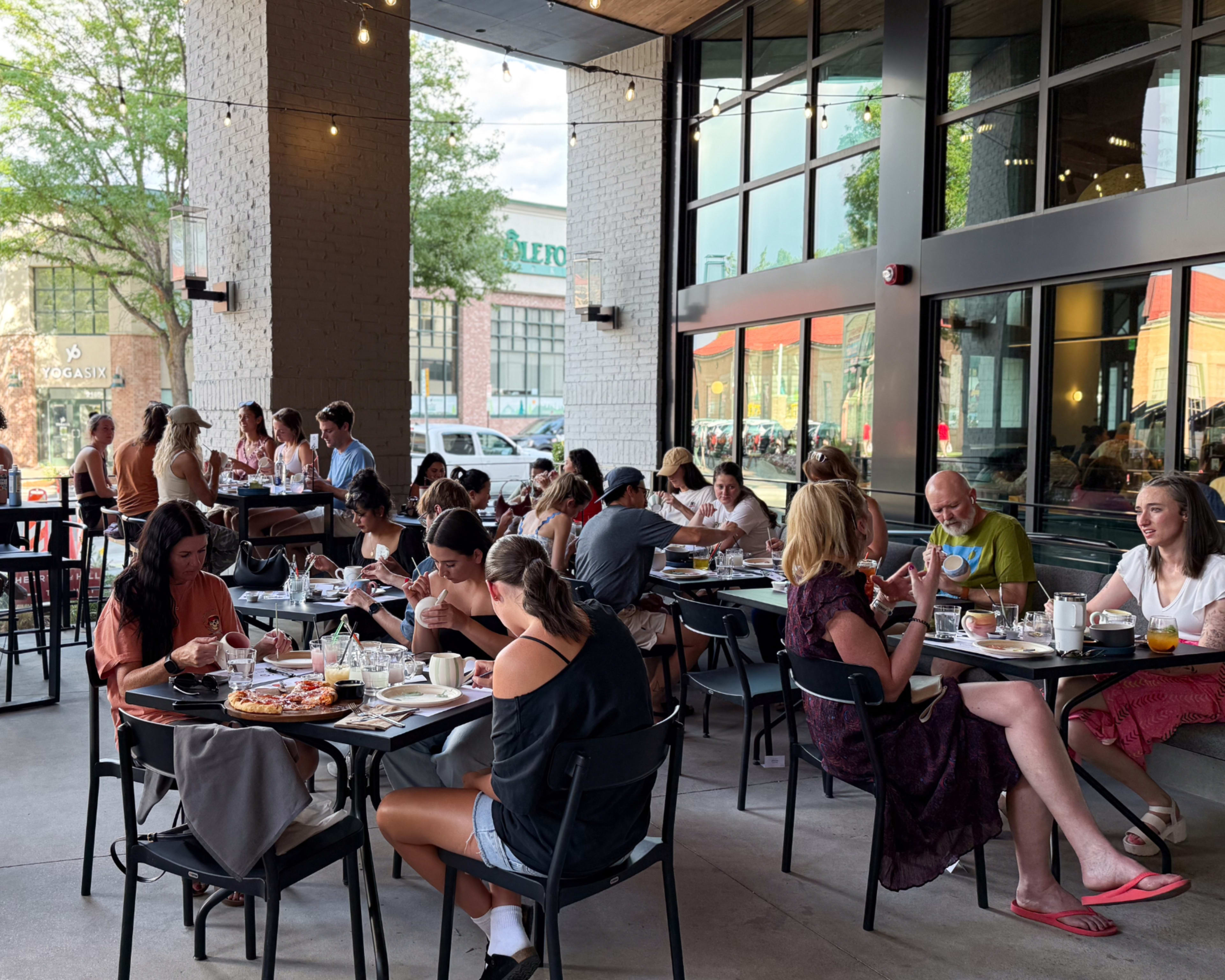 A bustling crowd enjoys meals and drinks at outdoor tables of a restaurant, with several groups engaged in conversation.