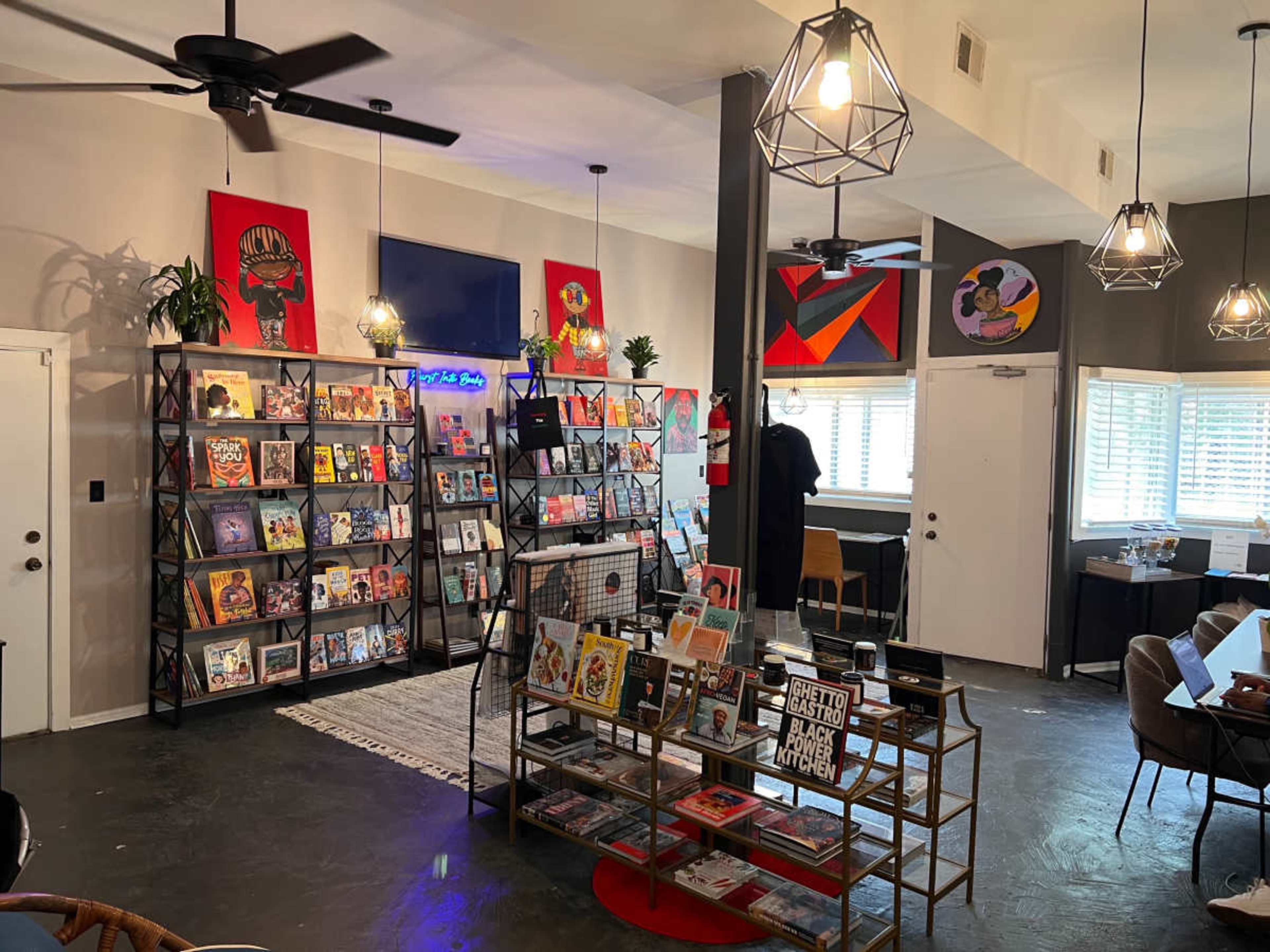 The image shows a modern bookstore featuring bookshelves filled with various titles, decorative art on the walls, and a cozy seating area.