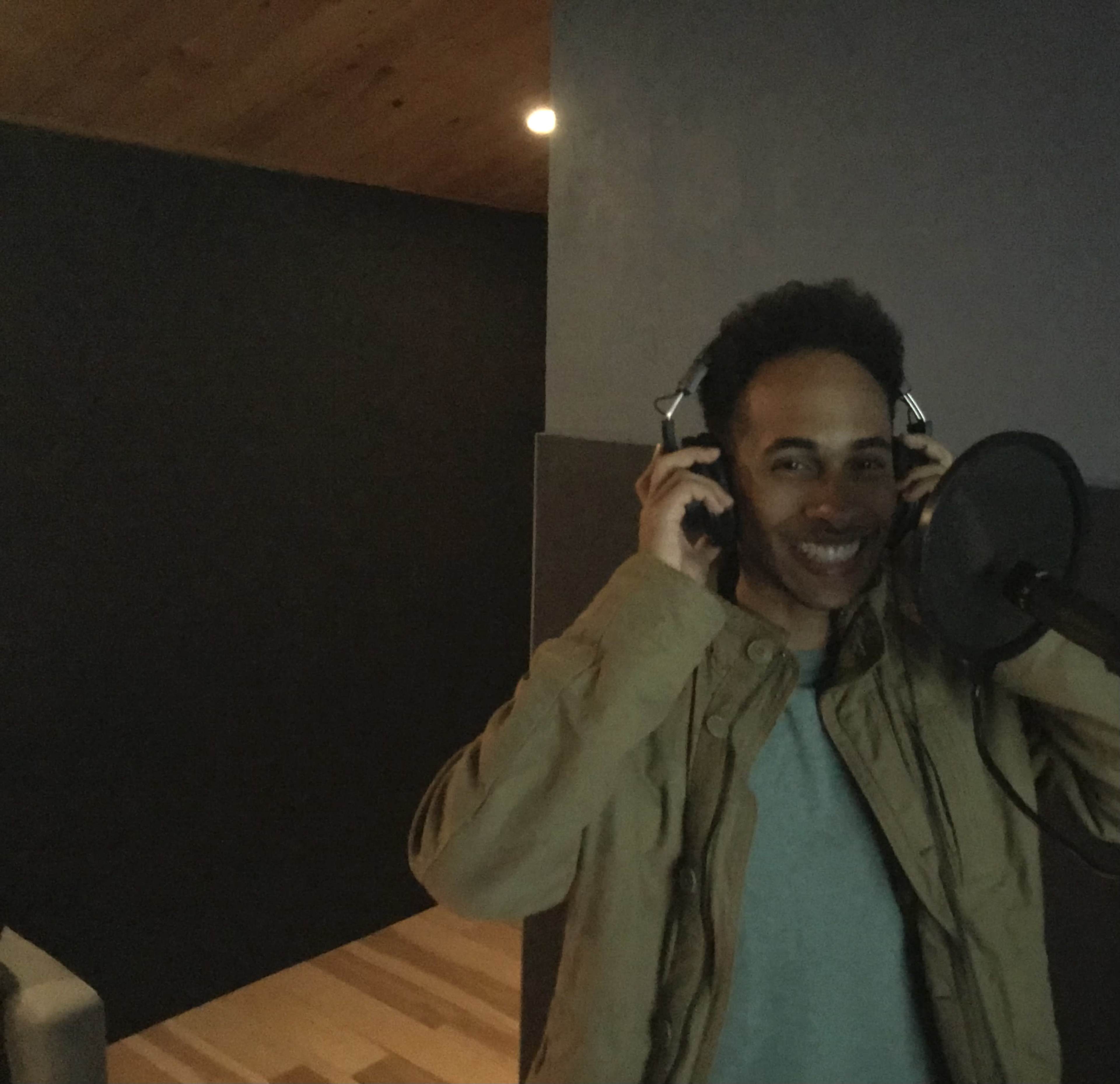 A person is wearing headphones and smiling while standing in a recording studio.