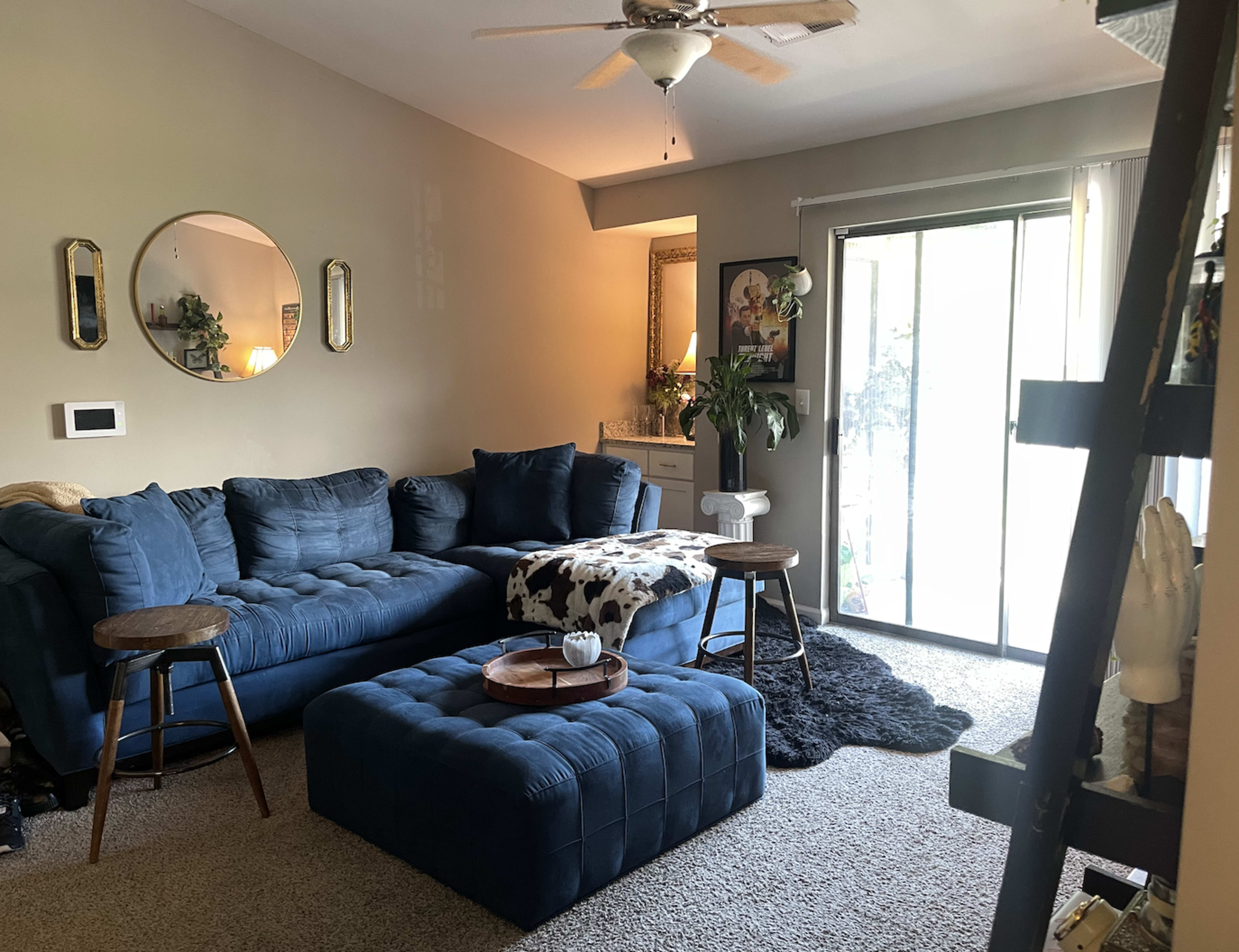 The living room features a blue sectional sofa, a matching ottoman, and a sliding glass door leading to a patio.