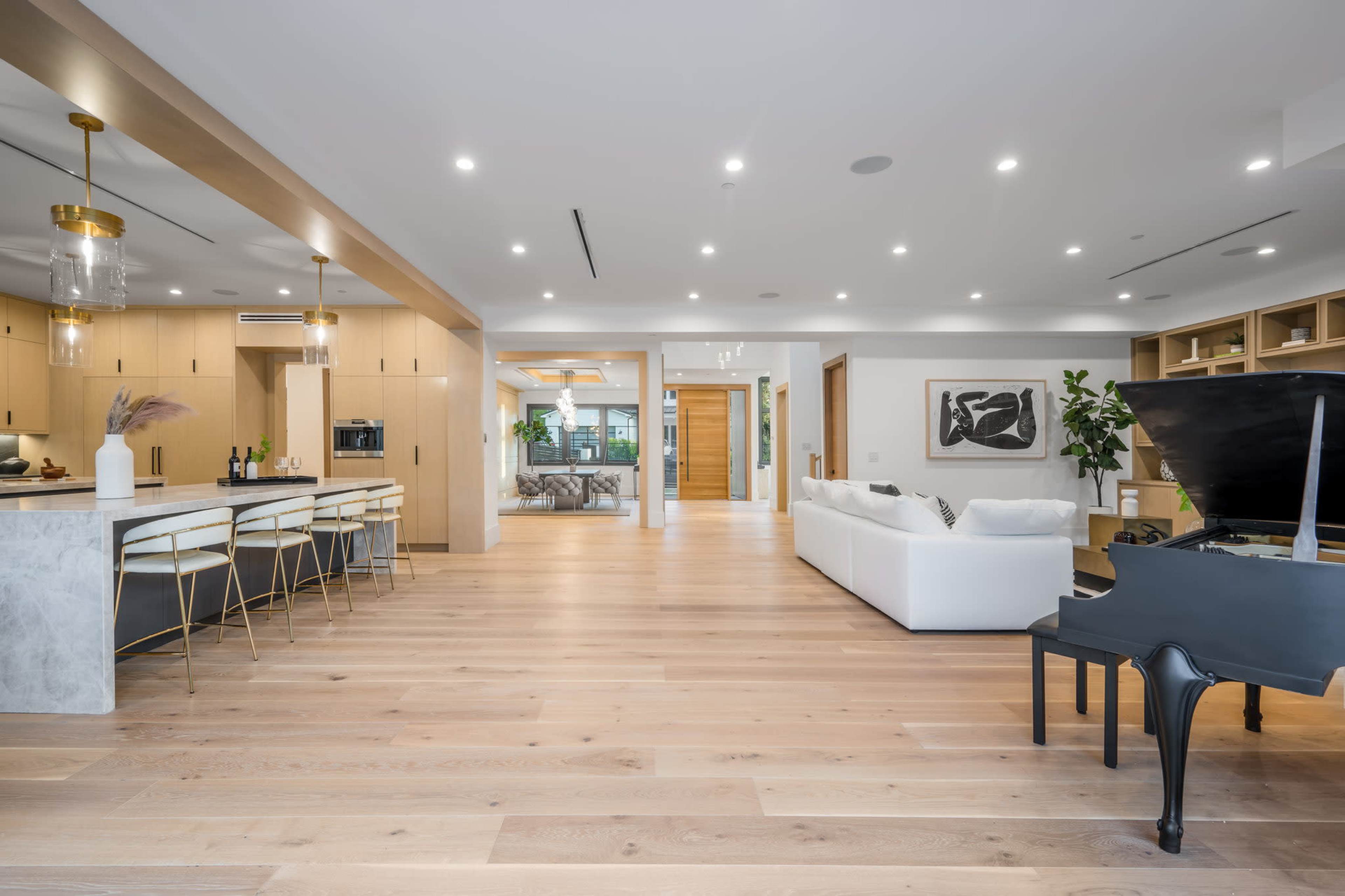 An open-concept living area featuring a modern kitchen with a countertop, a sleek dining space, a piano, and a spacious lounge area with white furniture.