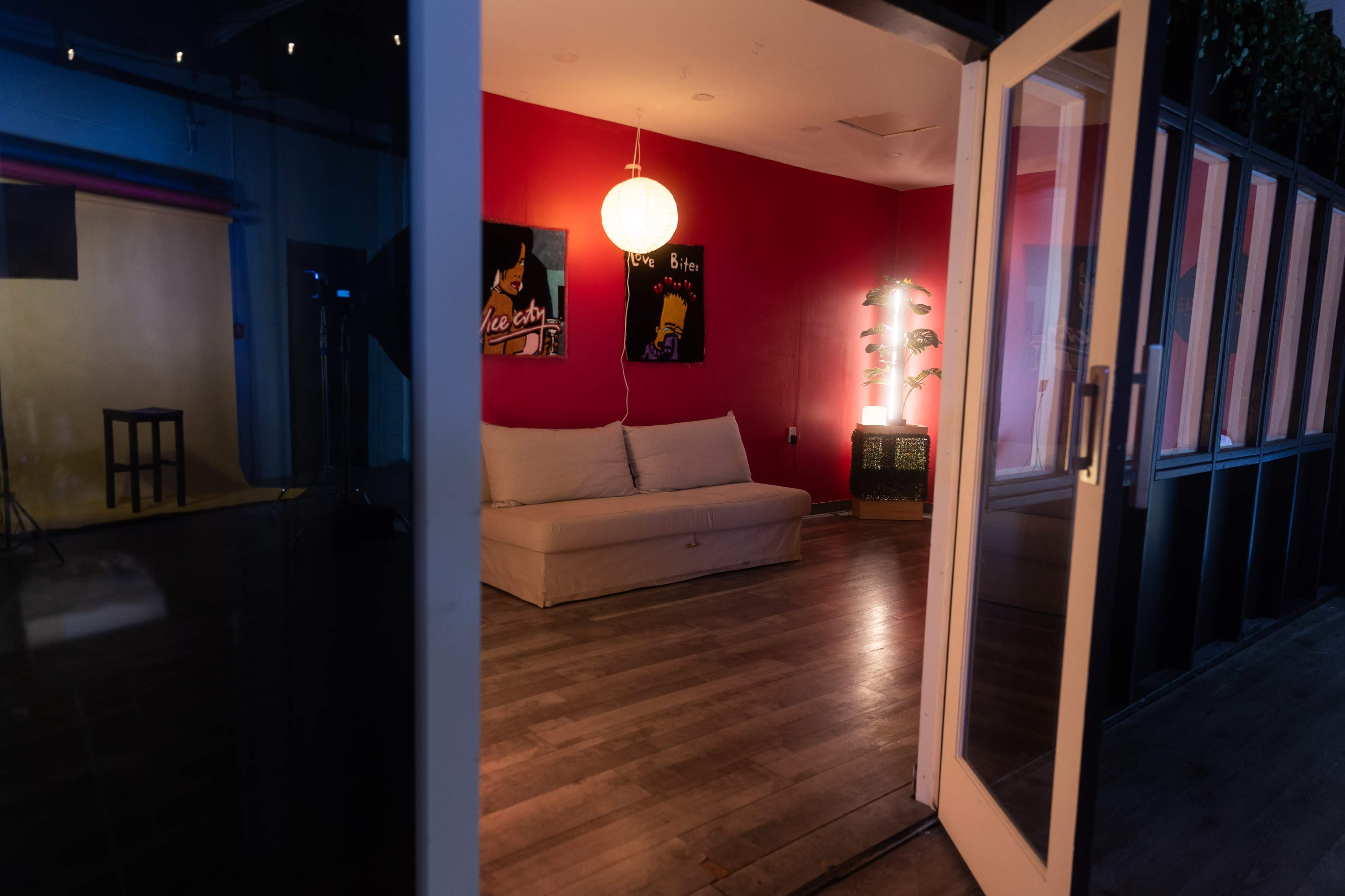 The image depicts a minimalist interior space with a red wall, a white sofa, and a round pendant light, accessed through glass doors.