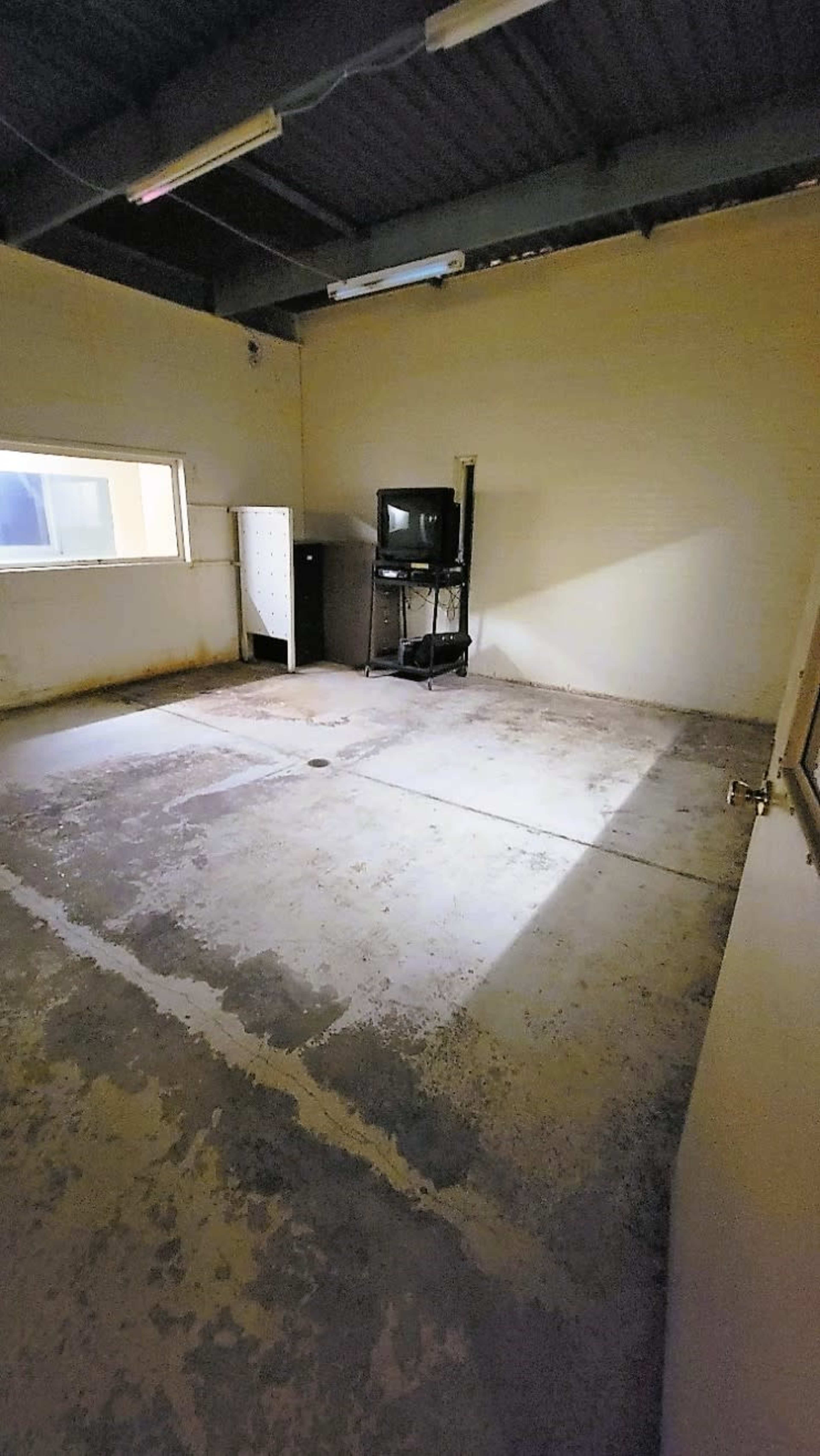 A sparse, empty room with concrete flooring, a window, and a television on a stand.