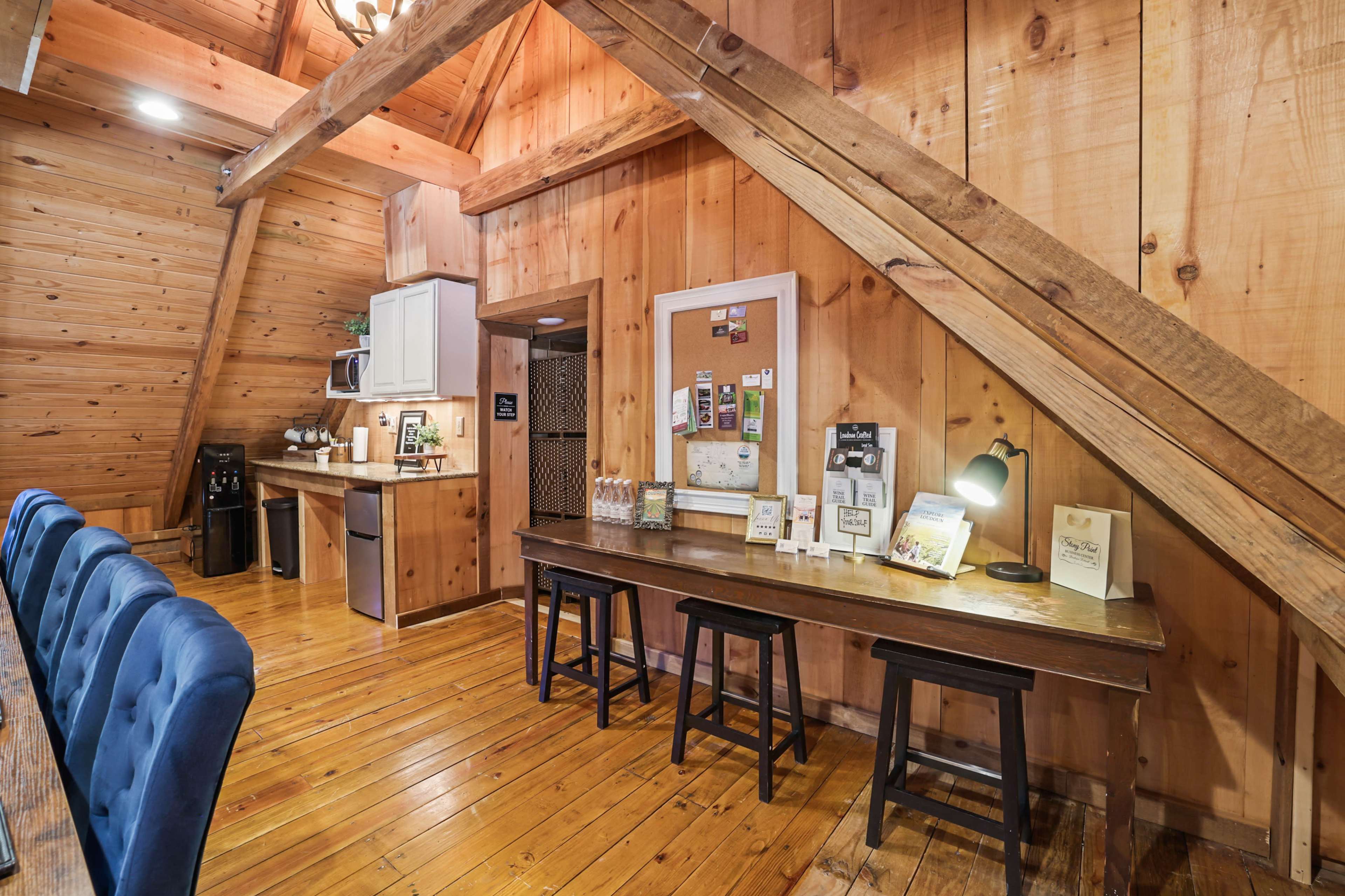 A wooden interior of a cabin with a long table, stools, and a kitchenette area against one wall.
