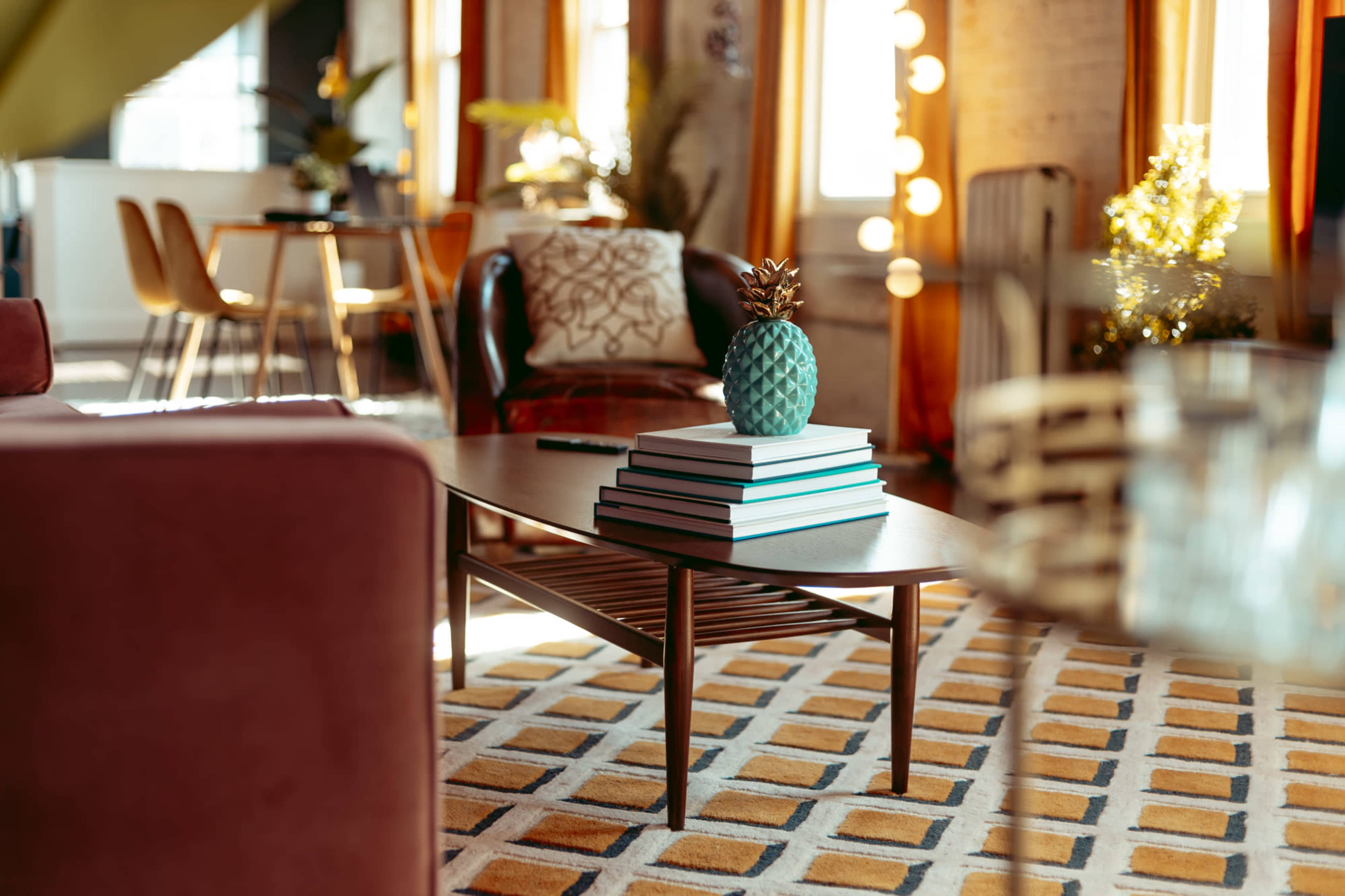 A modern living space with a coffee table stacked with books and a decorative pineapple, surrounded by various seating options and warm lighting.