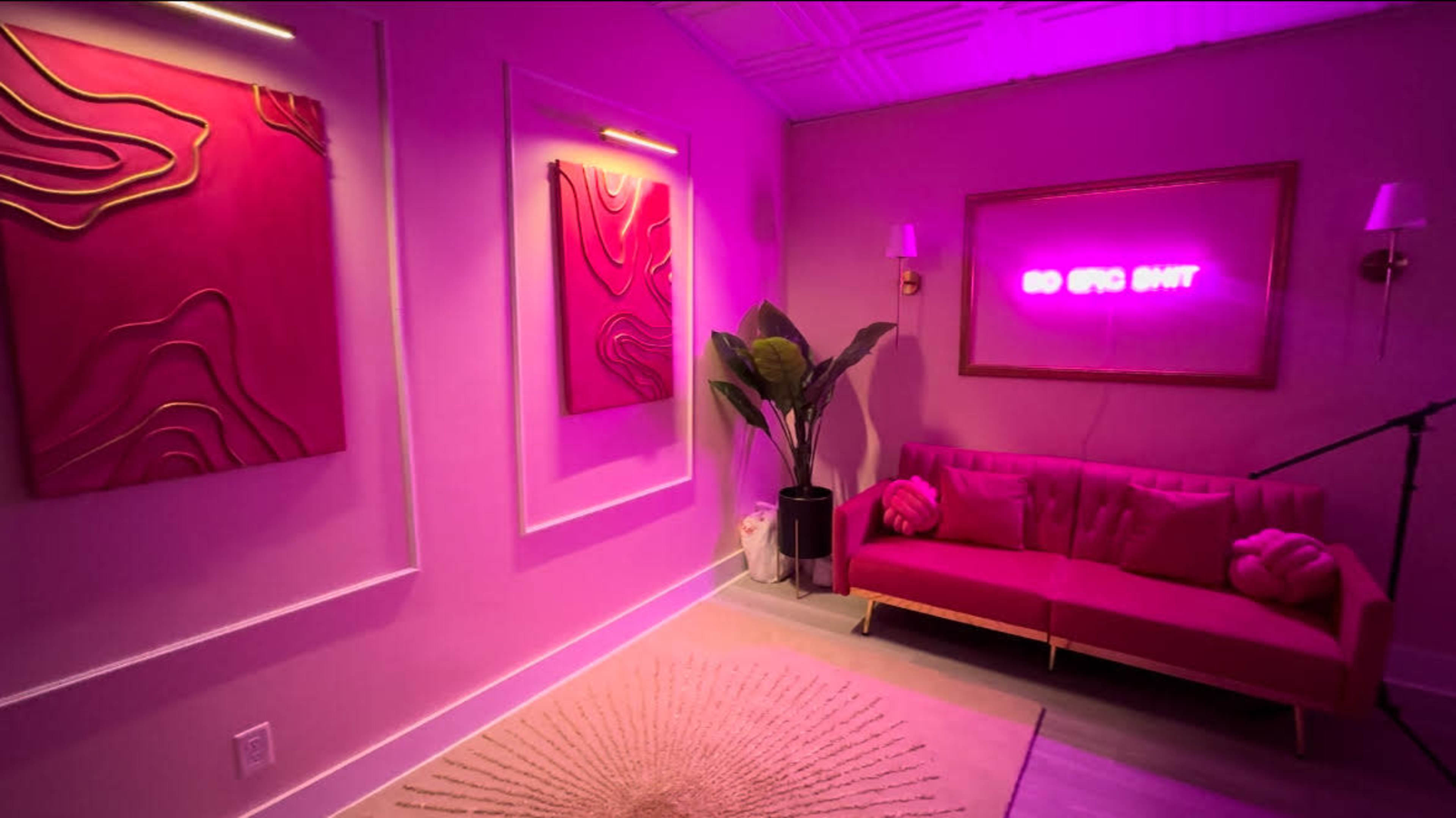 The image shows a modern room with pink wall art, a pink sofa, and a neon sign that reads "GO EPIC SHIT" illuminated against a pastel background.