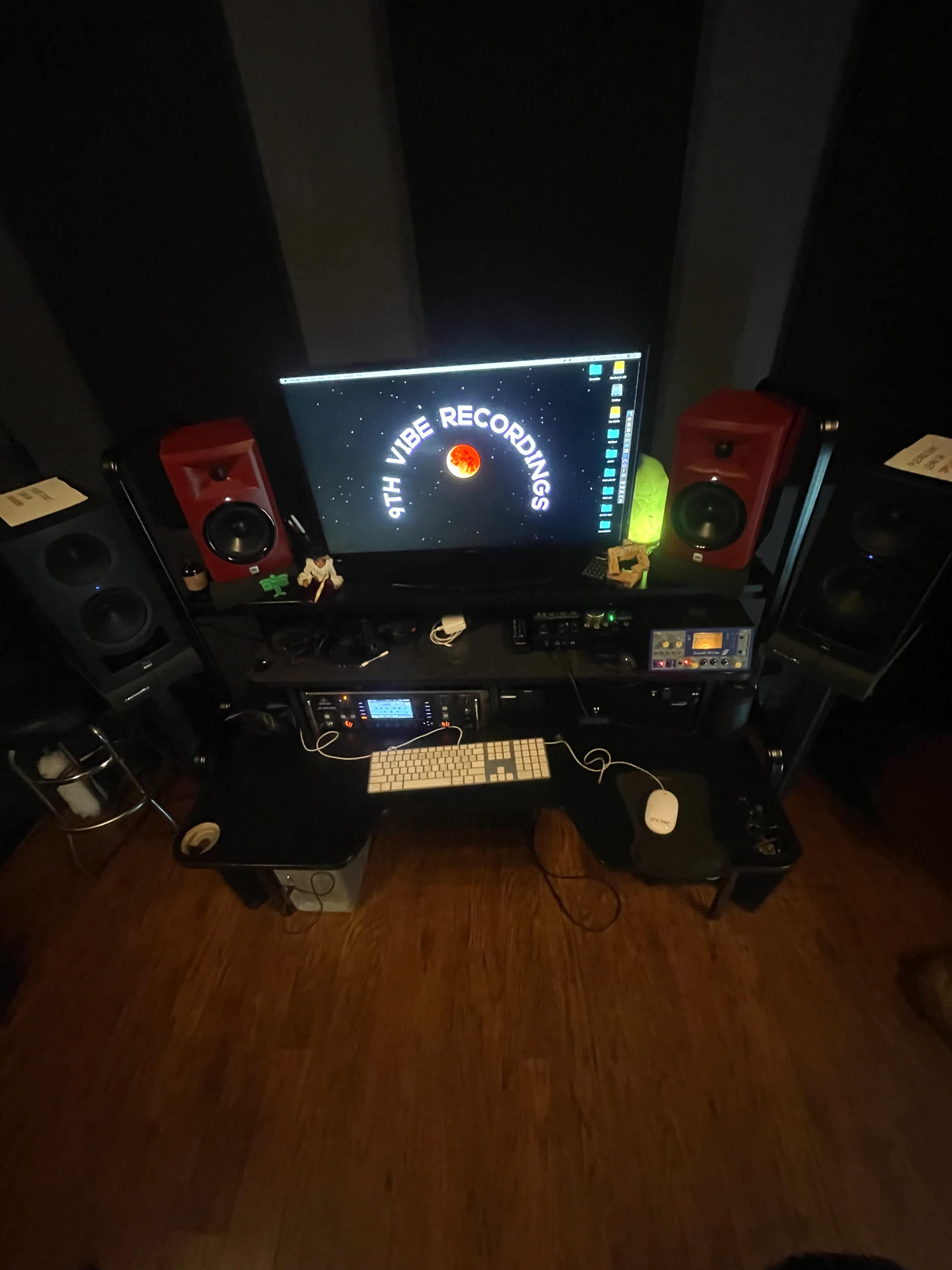 A music production studio setup featuring a computer monitor displaying "Earth Vibe Recordings," flanked by red studio monitors and a keyboard on a dark desk.