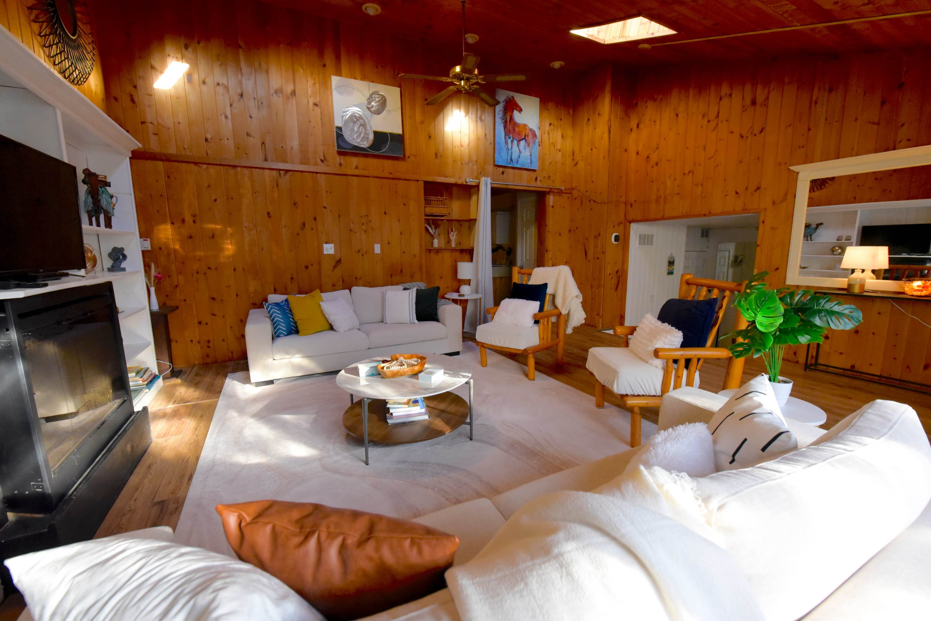 The living room features wooden walls, a circular coffee table at the center, and two armchairs arranged around a white sofa.