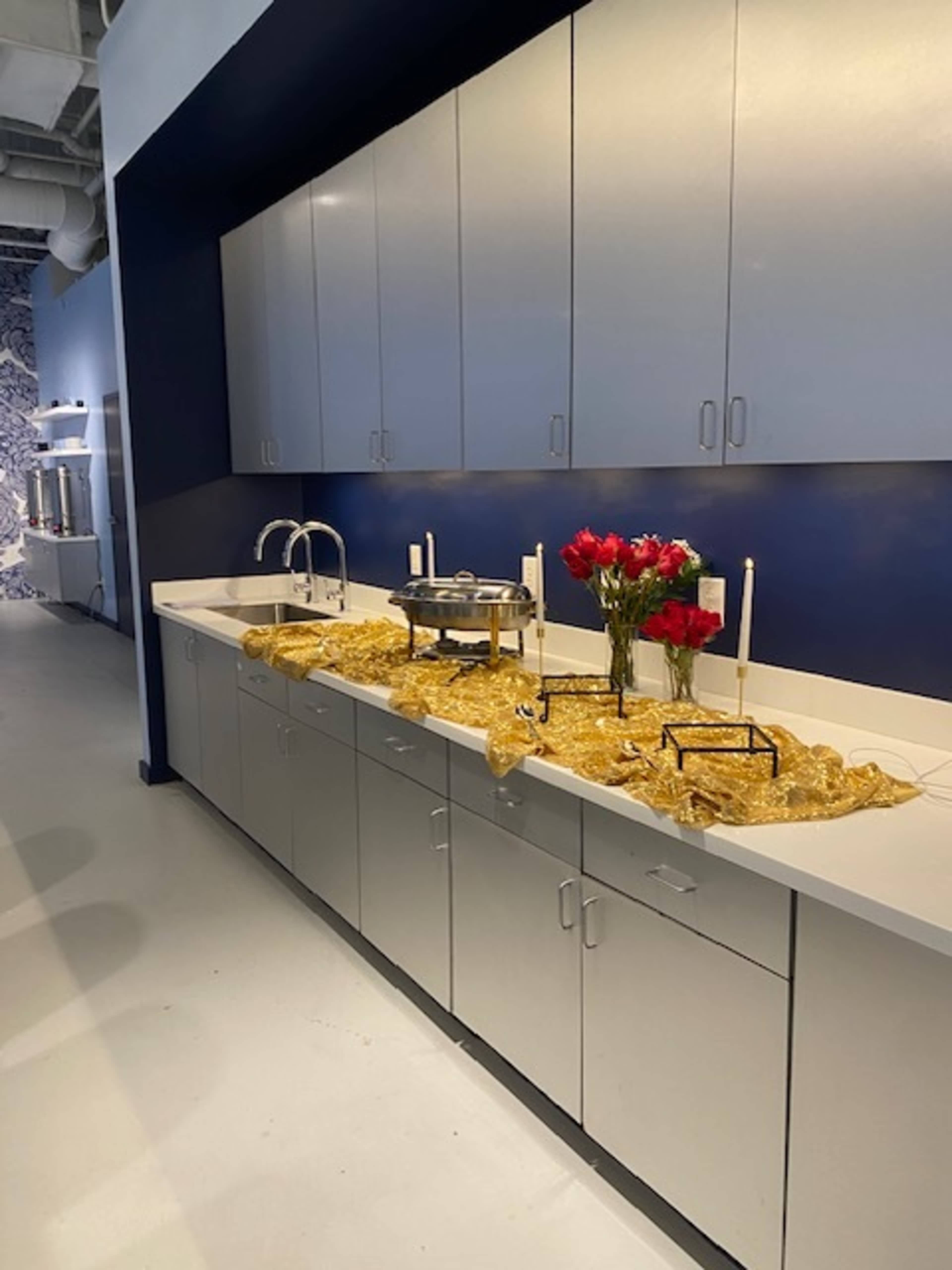 A modern kitchen with gray cabinets features a countertop adorned with a golden table runner, a floral arrangement of red roses, and two candelabras.