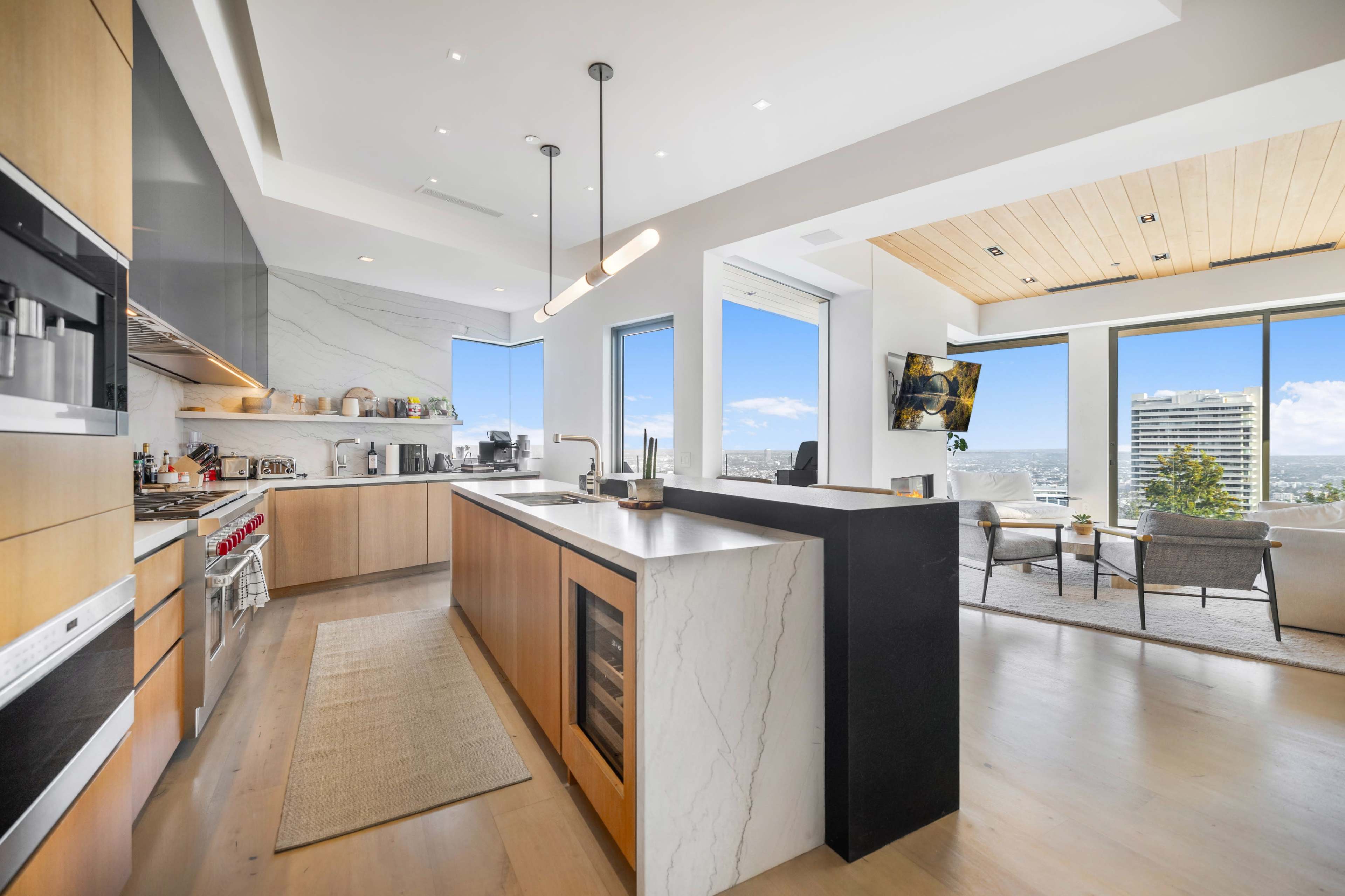 A modern kitchen features sleek cabinetry, a large island with a waterfall countertop, and expansive windows offering a city view.