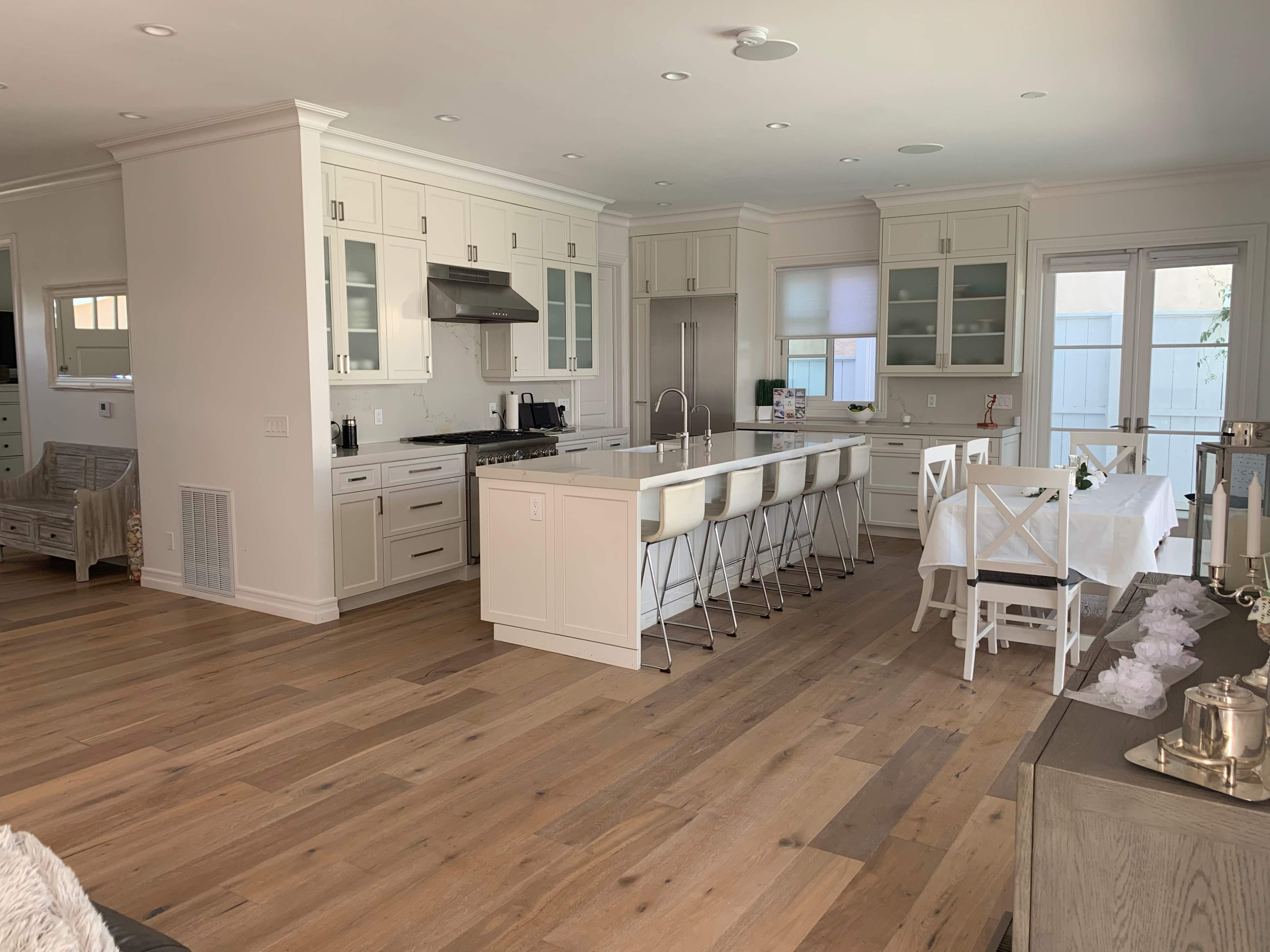 A modern kitchen and dining area with white cabinetry, a large island with bar stools, and a white dining table set for meals.