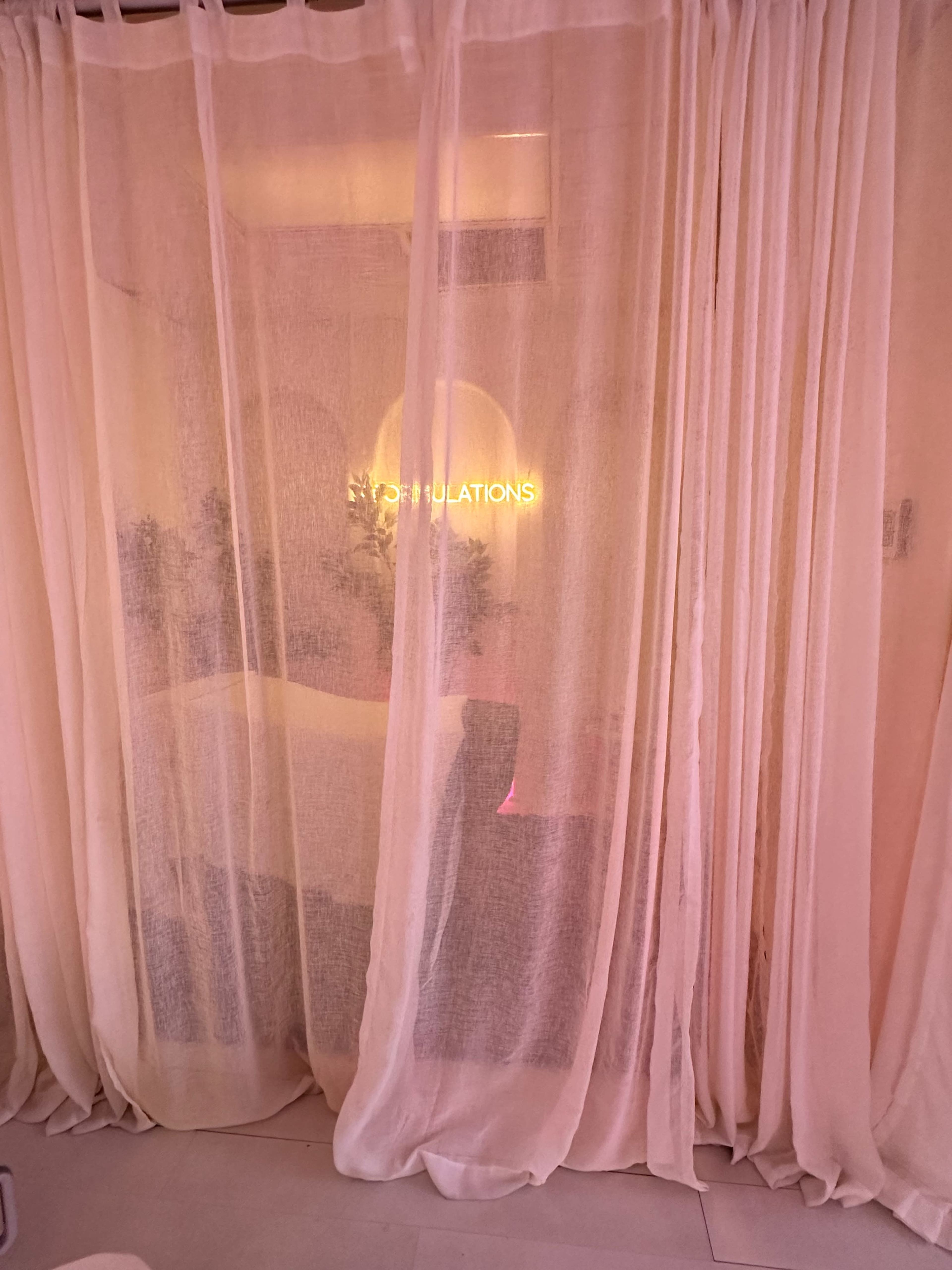 The image shows sheer curtains in a softly lit space with the words "Congratulations" illuminated behind them.