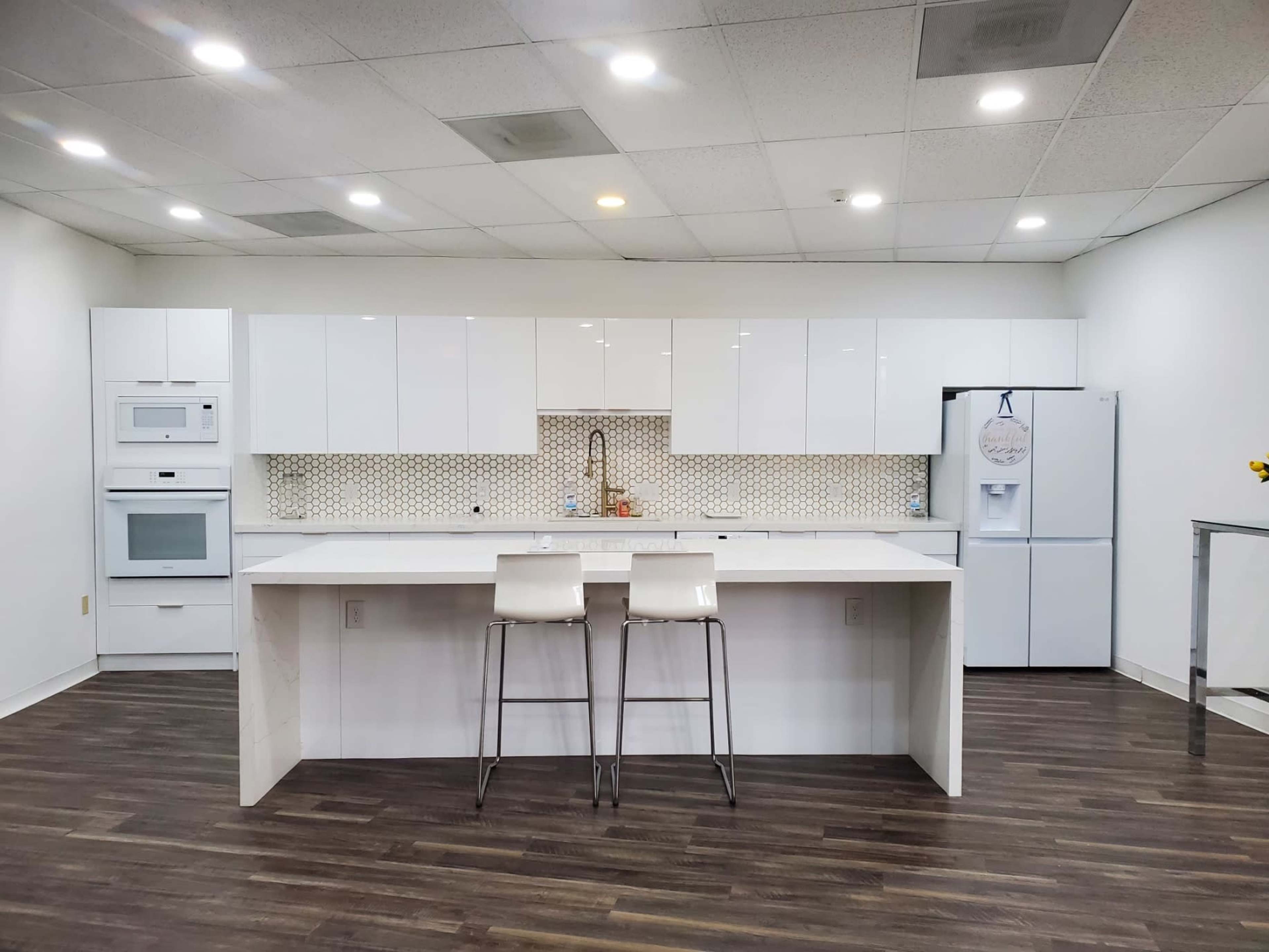 A modern kitchen features white cabinetry, a patterned backsplash, and a central island with two stools.