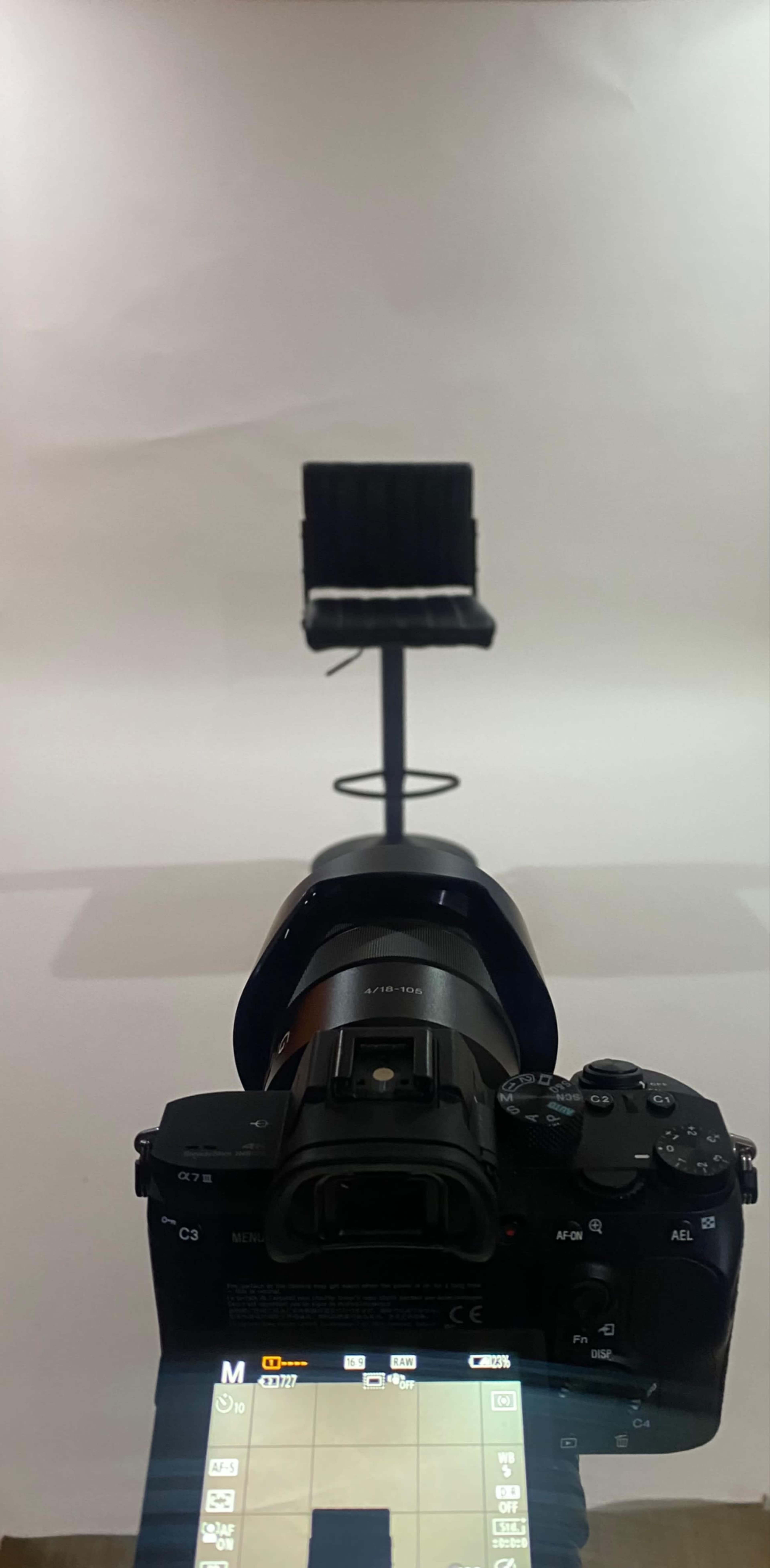 A camera is positioned in front of a black swivel chair against a plain white background.