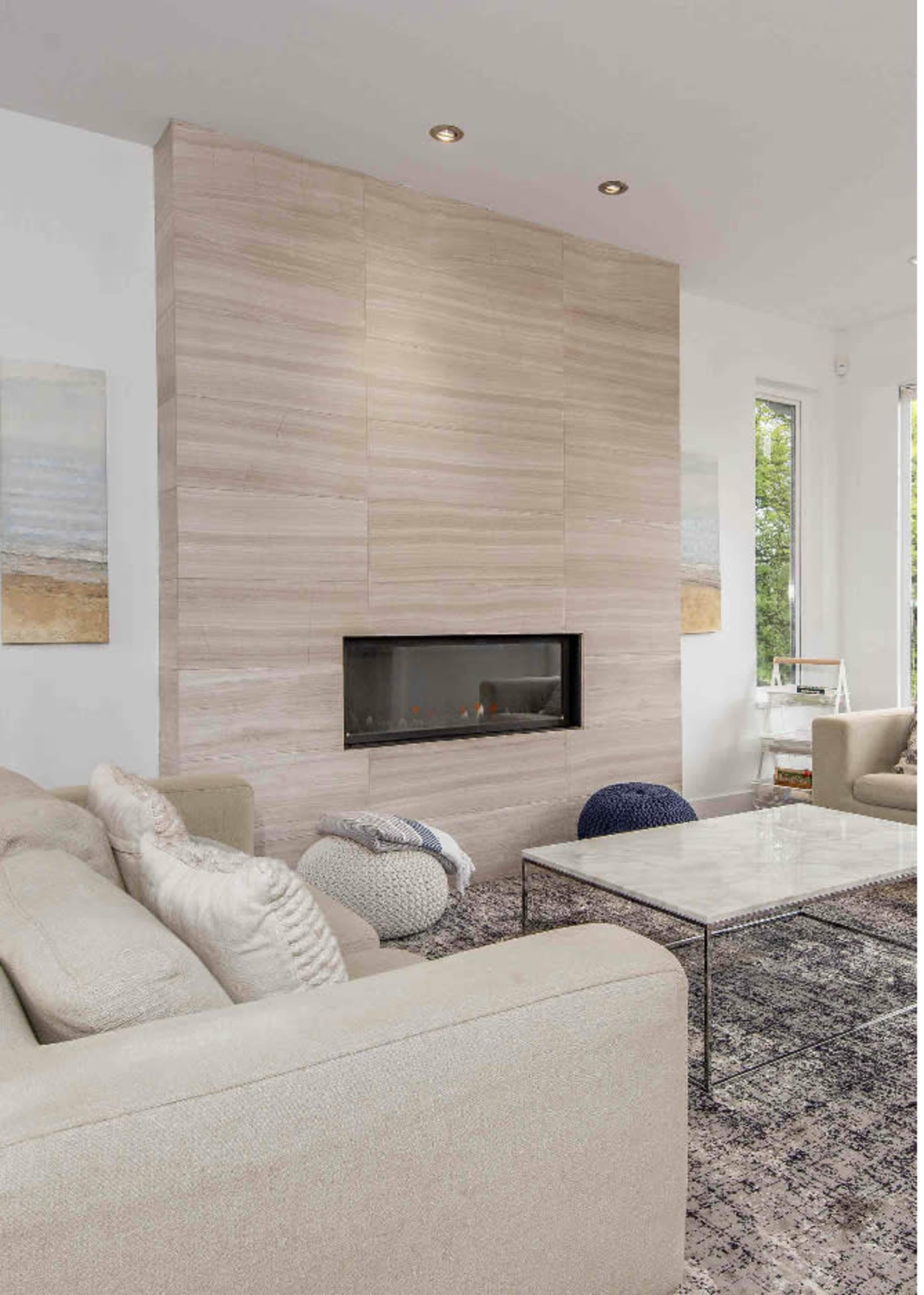 A modern living room features a sleek, light-colored stone fireplace, a low coffee table, and comfortable sofas arranged on a patterned rug.