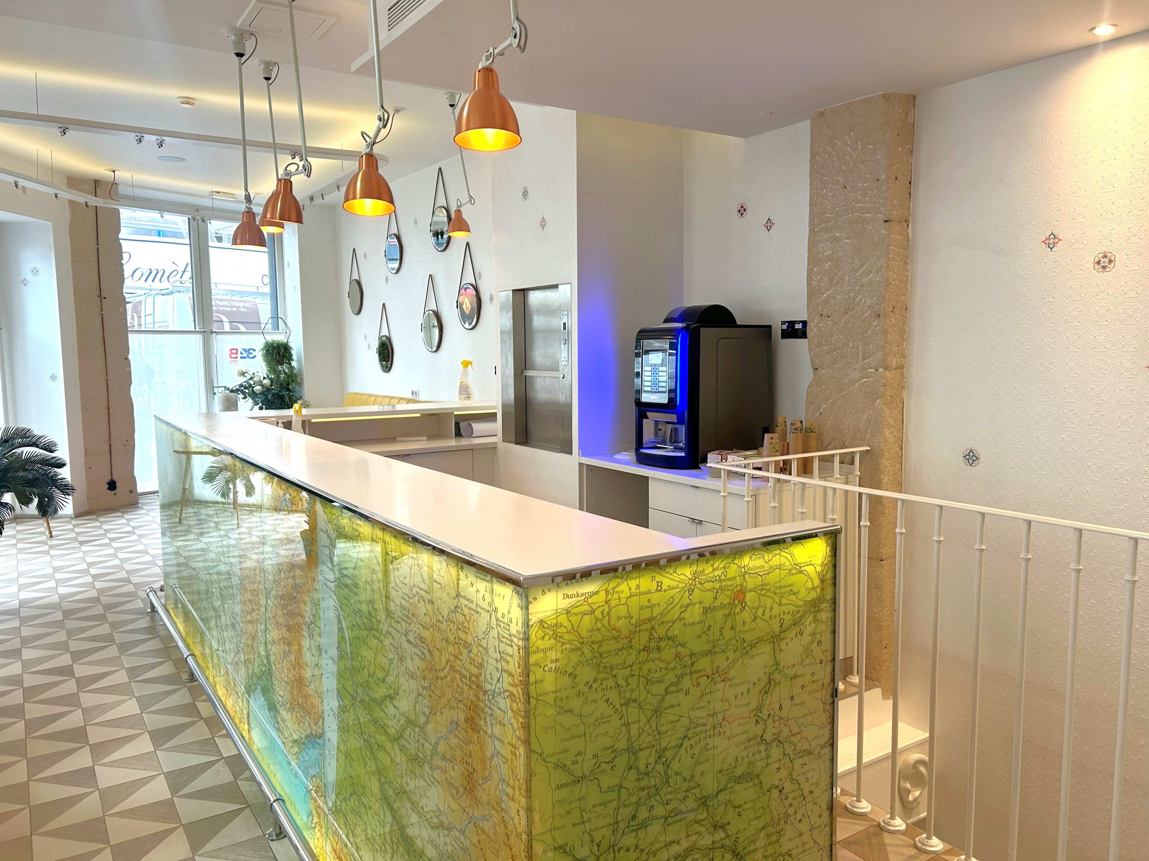 A brightly lit reception area features a sleek white counter with a translucent map design and hanging pendant lights.