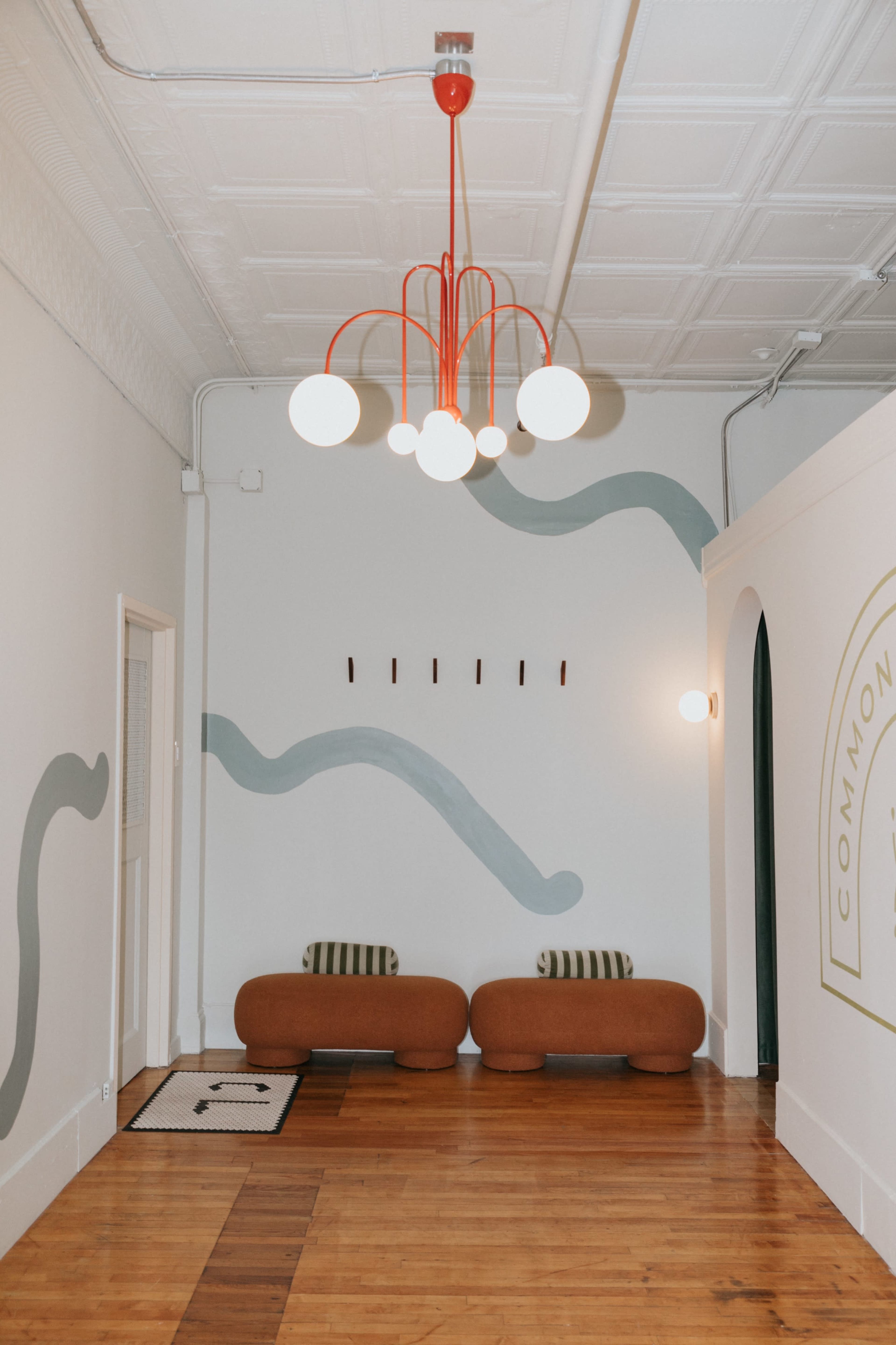 The image shows a room with two brown benches, a stylish chandelier with white globes and red accents, and patterned walls featuring wavy green designs.
