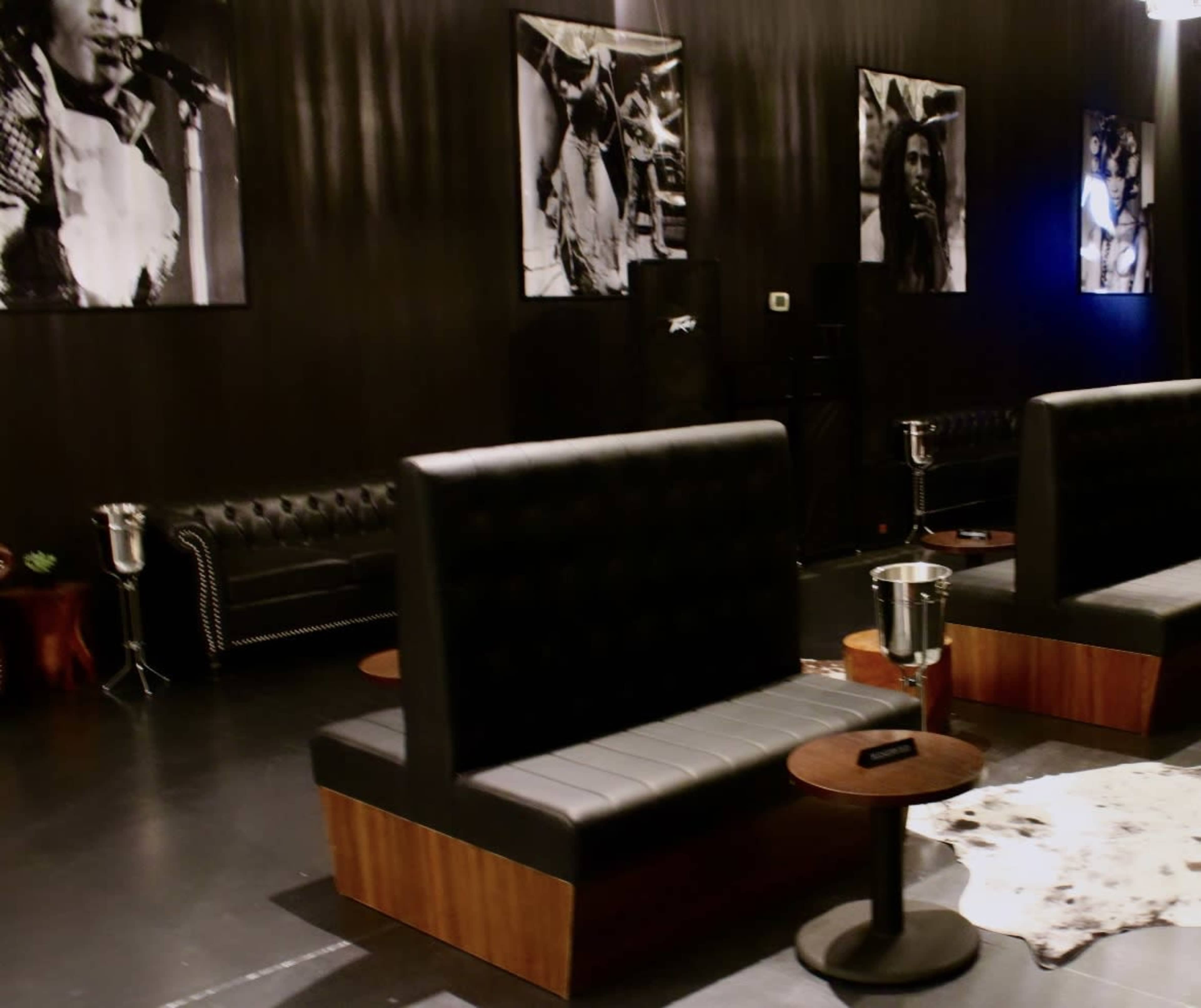A dimly lit lounge area featuring black leather couches, low tables, and large photographs on the walls.
