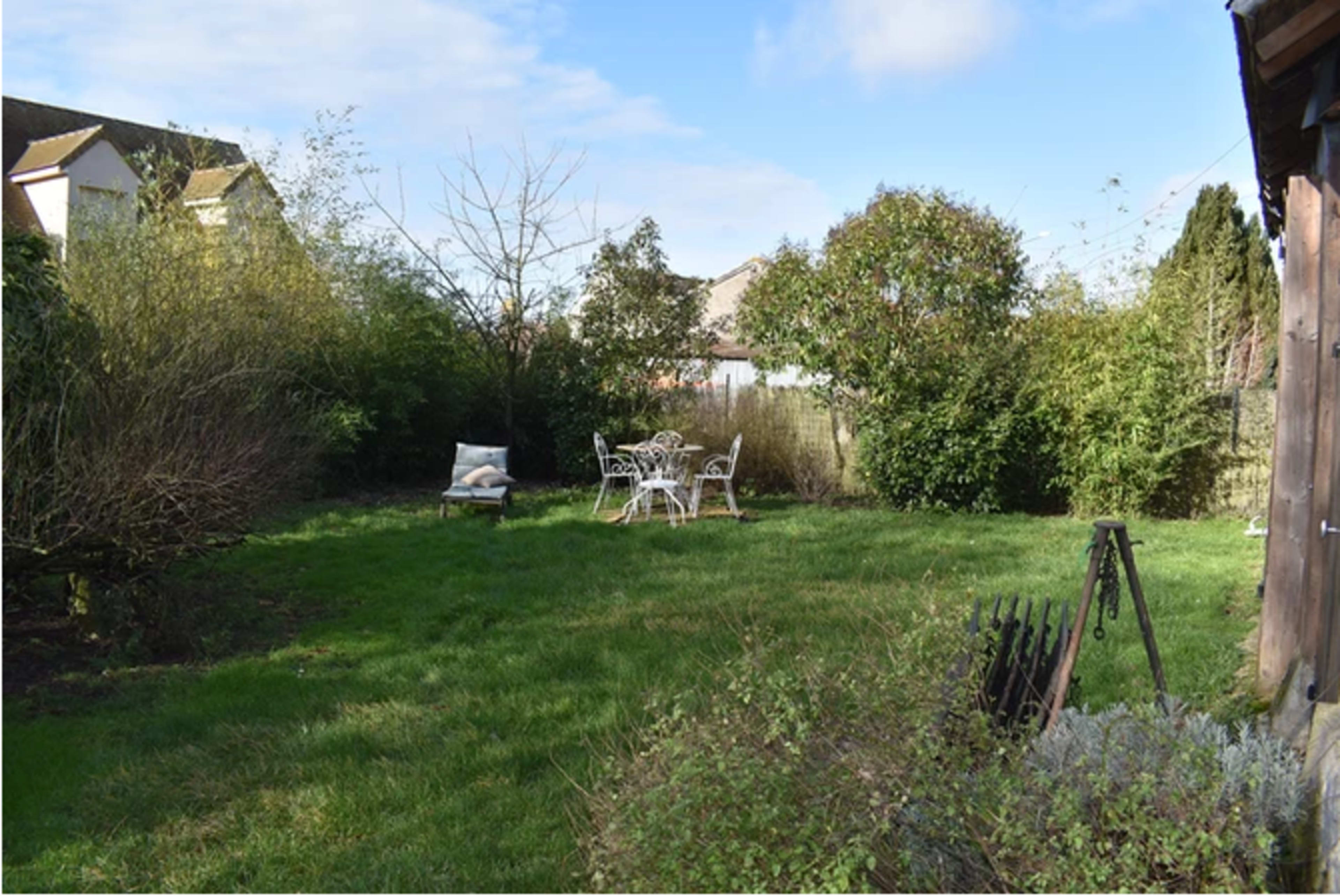 A grassy garden area with a small seating arrangement and surrounding shrubs and trees.