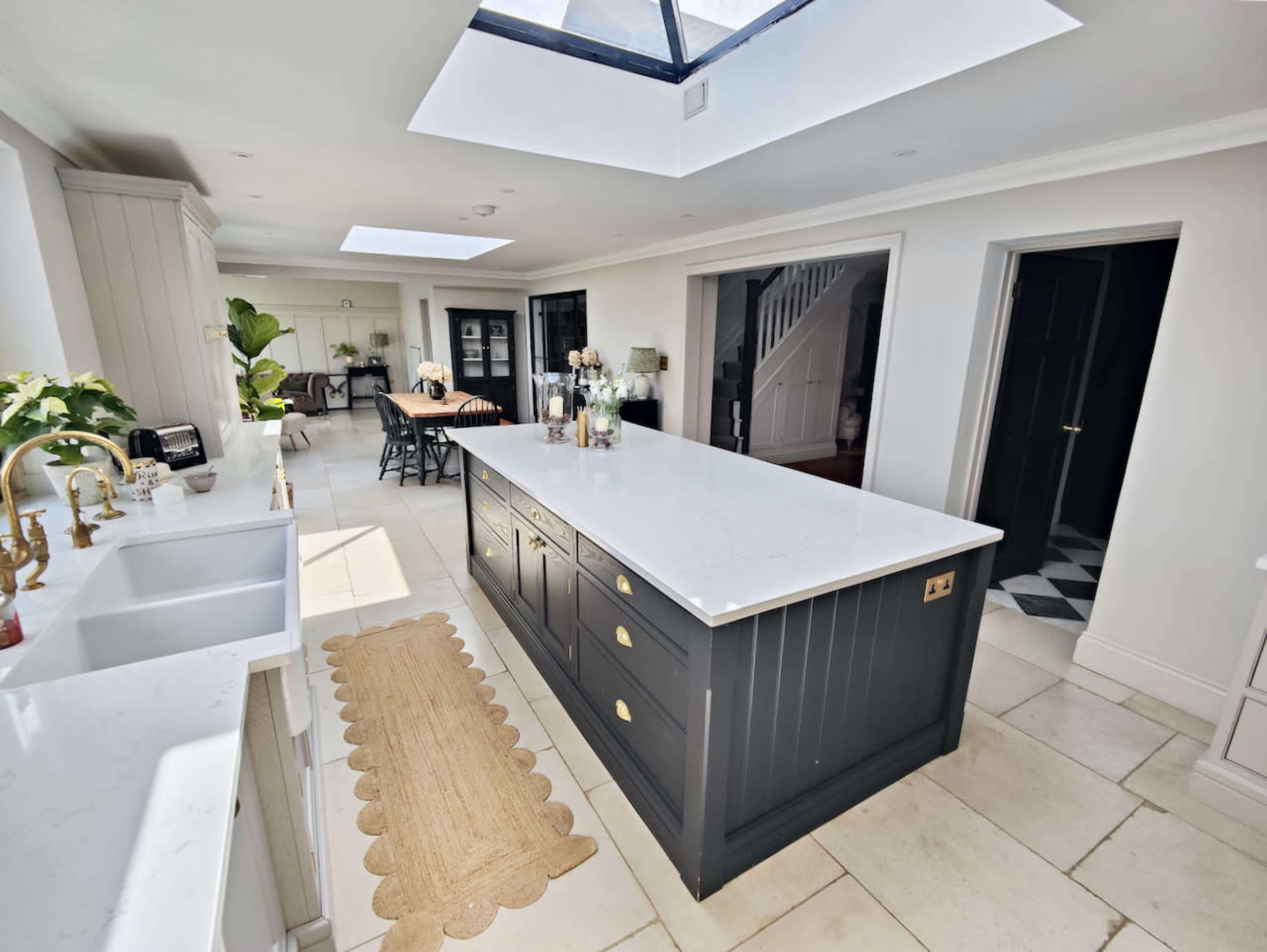 The kitchen features a large central island with a marble countertop, surrounded by light-colored cabinetry and illuminated by a skylight.