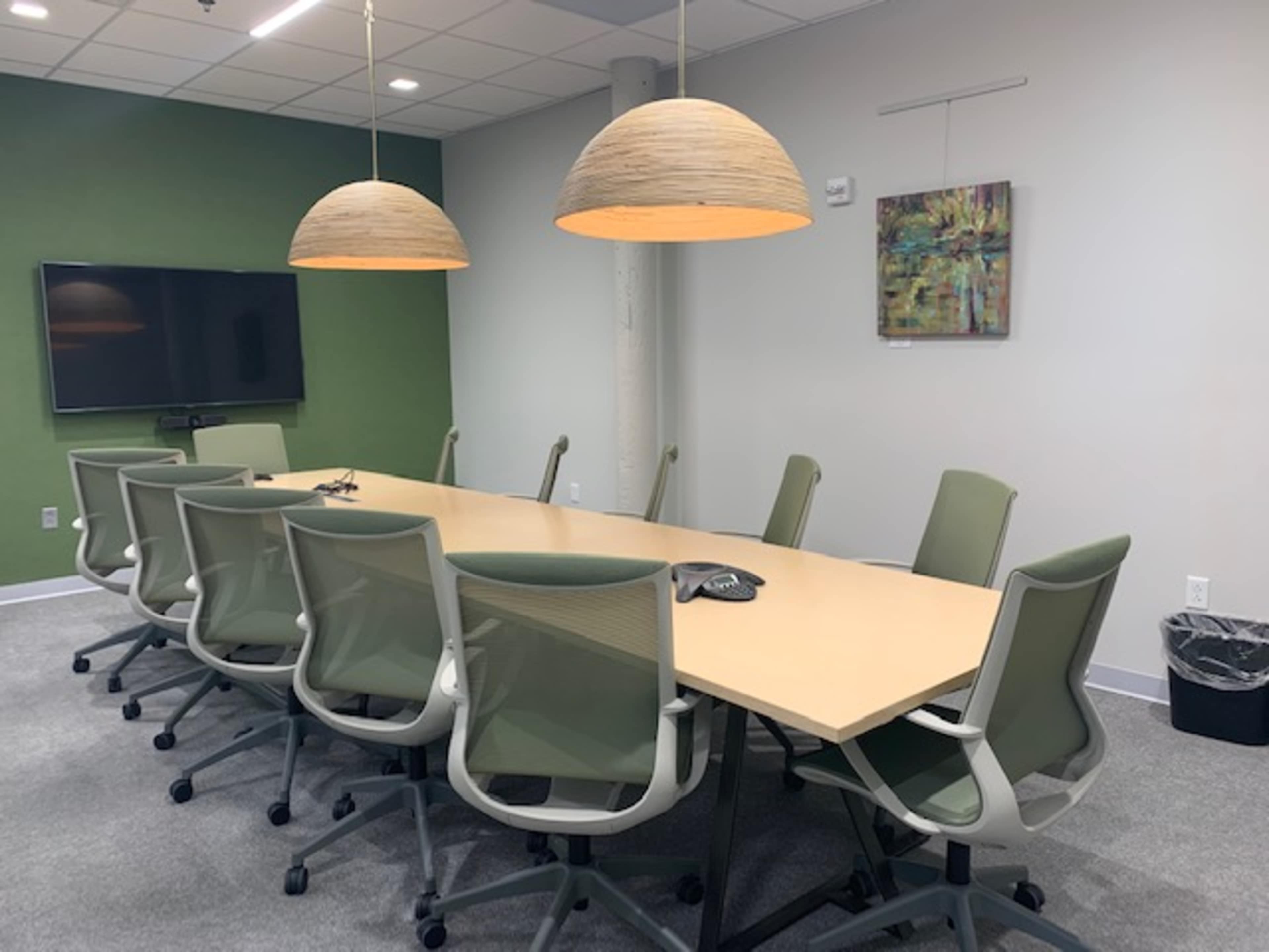 A conference room with a long table, green chairs, and two pendant lights hanging above it.