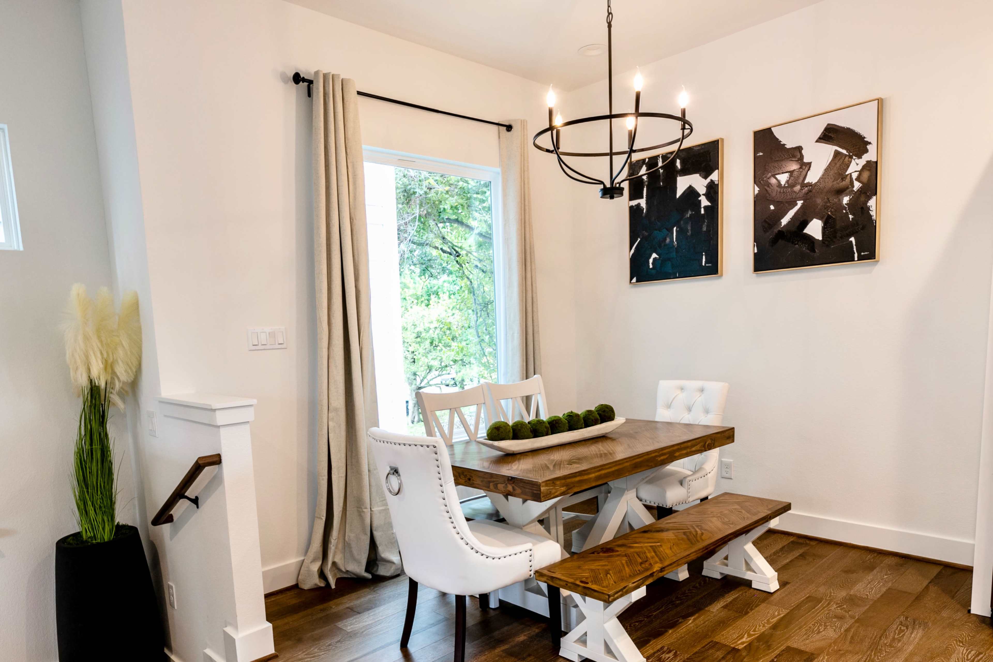 A modern dining area featuring a wooden table with white chairs, a chandelier overhead, and two abstract paintings on the wall.