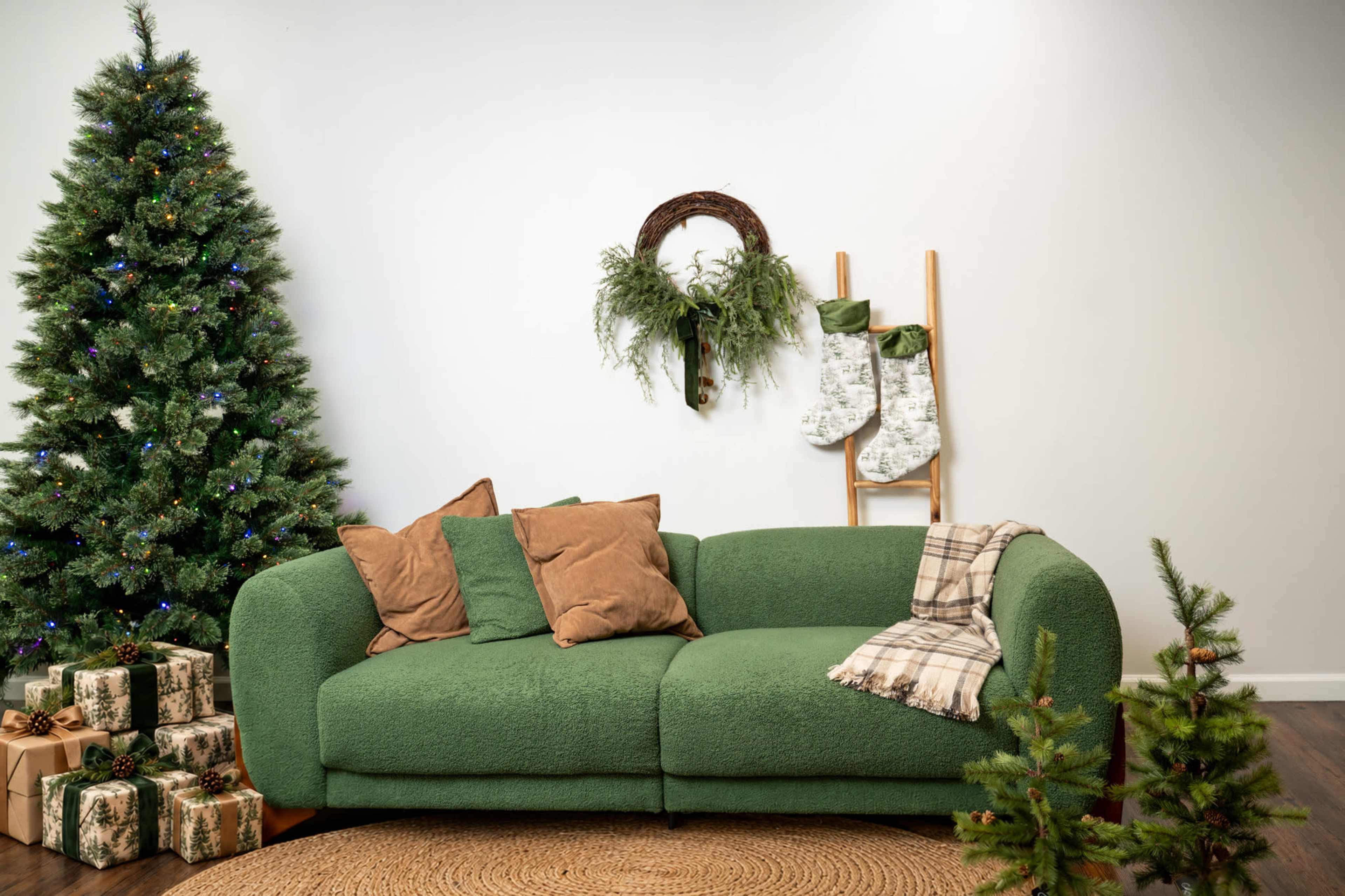 The image features a green sofa with brown pillows, surrounded by a decorated Christmas tree, presents, a wreath, and stockings hanging from a ladder.
