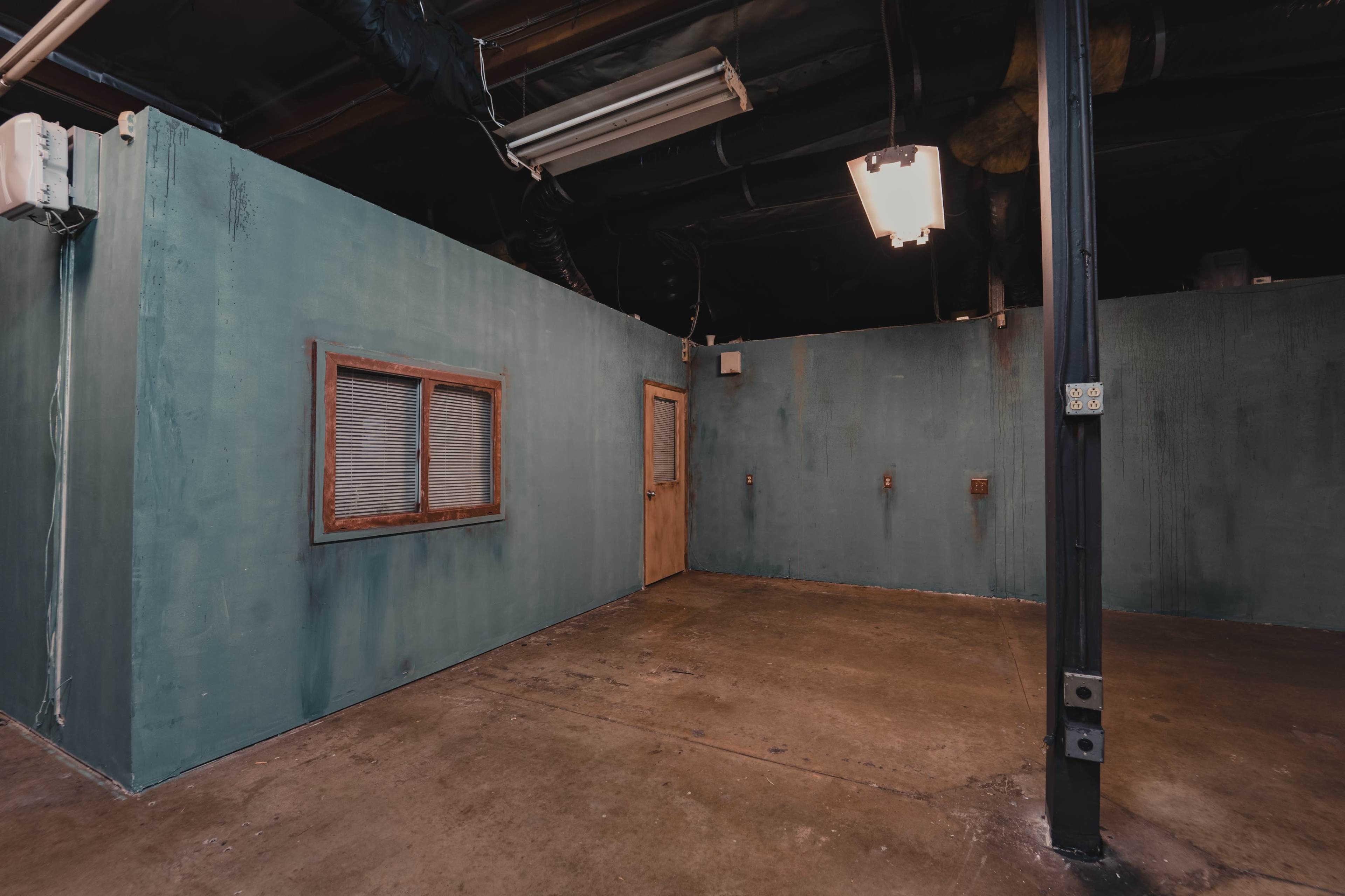 An empty room with teal walls, a window, a door, and concrete flooring.