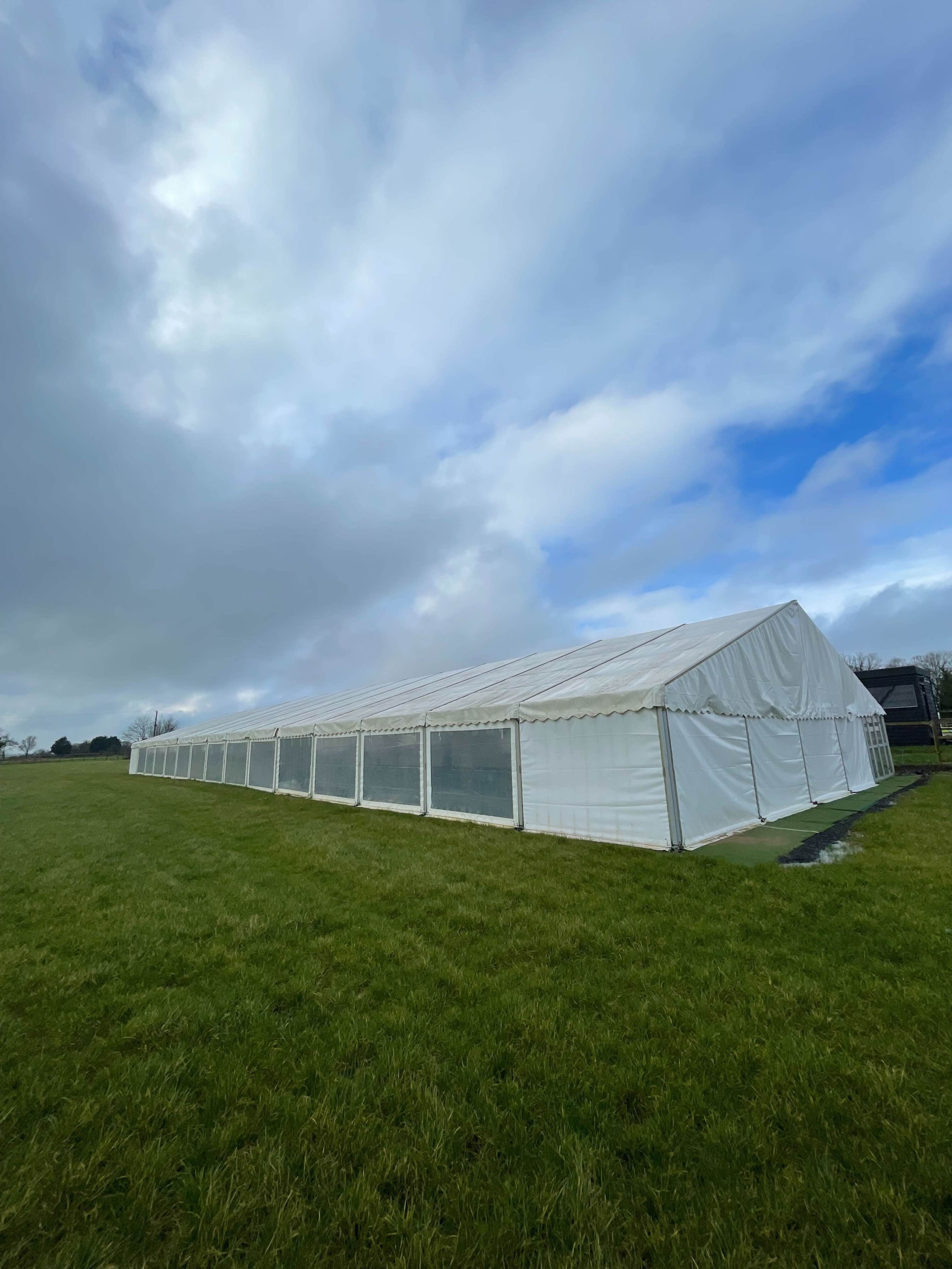 A large white tent is set up on a grassy field under a cloudy sky.