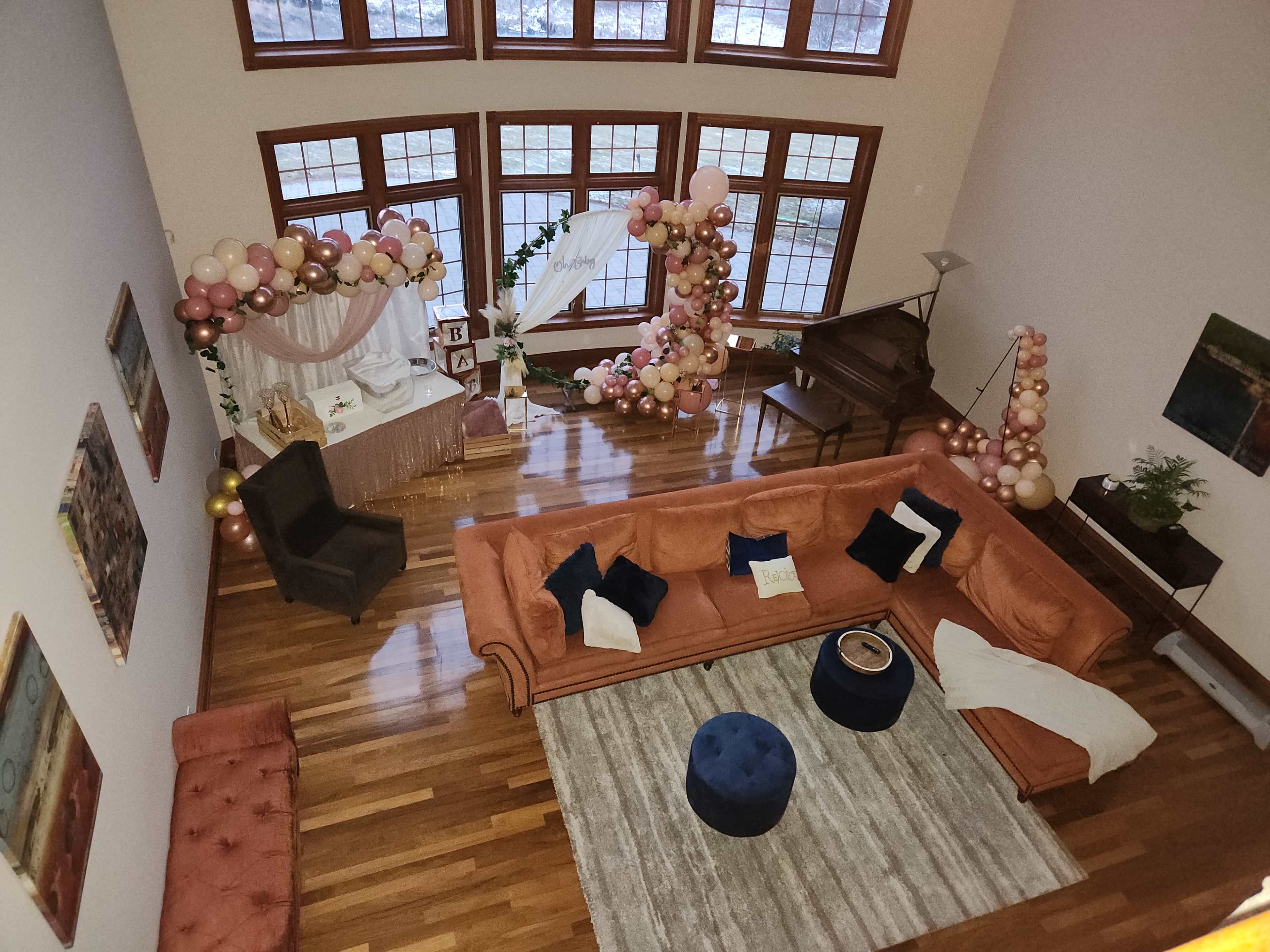 A spacious living room with a large orange sectional sofa, a round blue ottoman, and a decorated corner featuring a balloon arch and a table set up for an event.